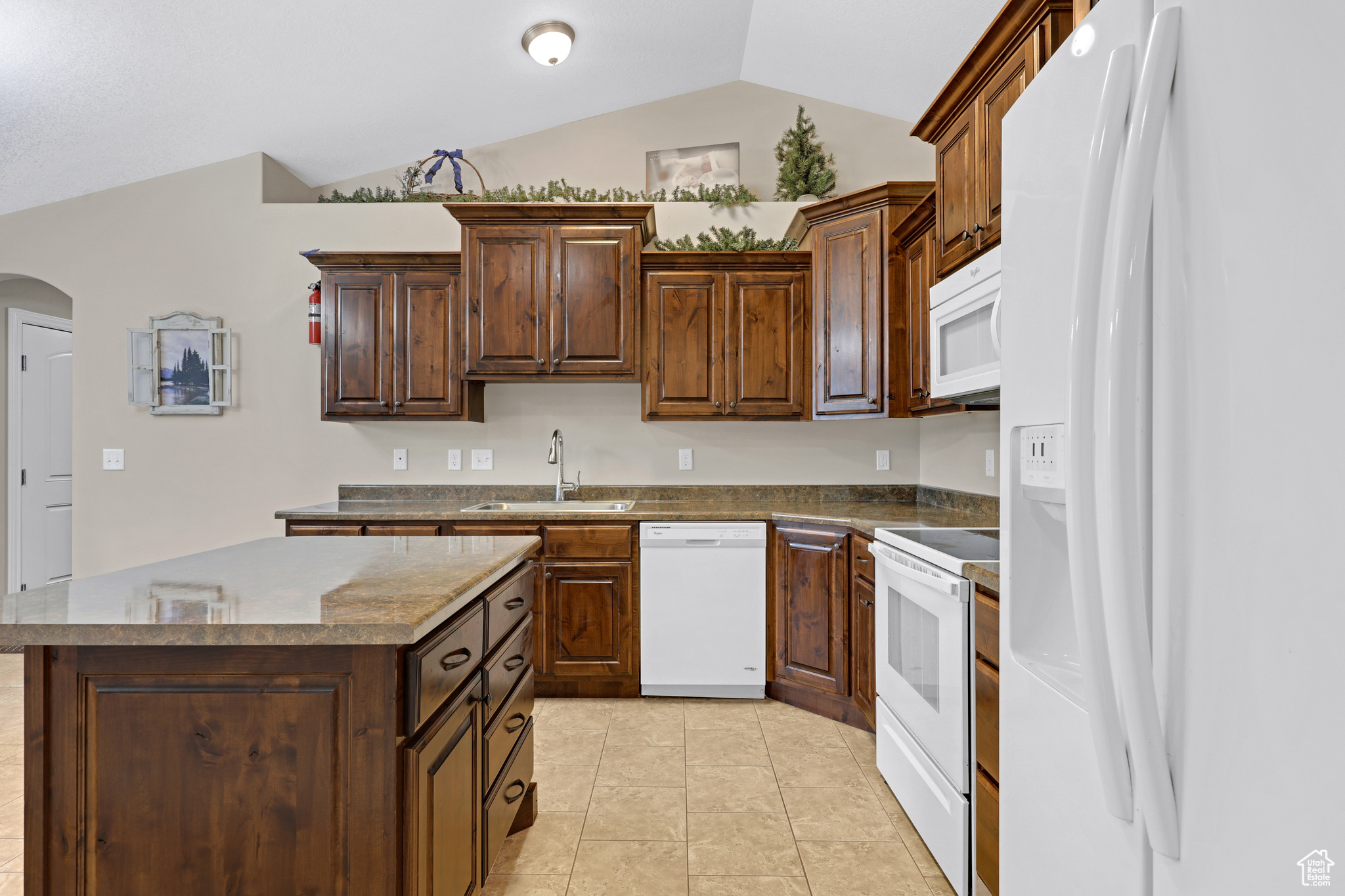 Kitchen featuring sink, a center island, lofted ceiling, white appliances, and light tile patterned floors