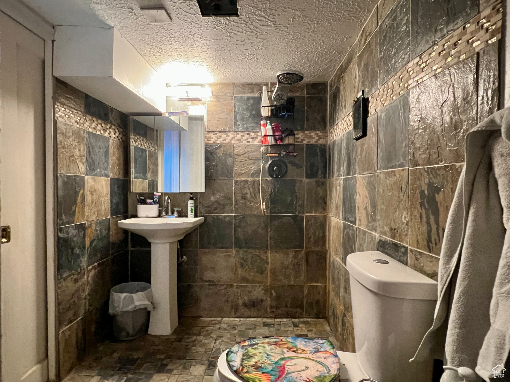 Bathroom with toilet, a textured ceiling, a shower, and tile walls