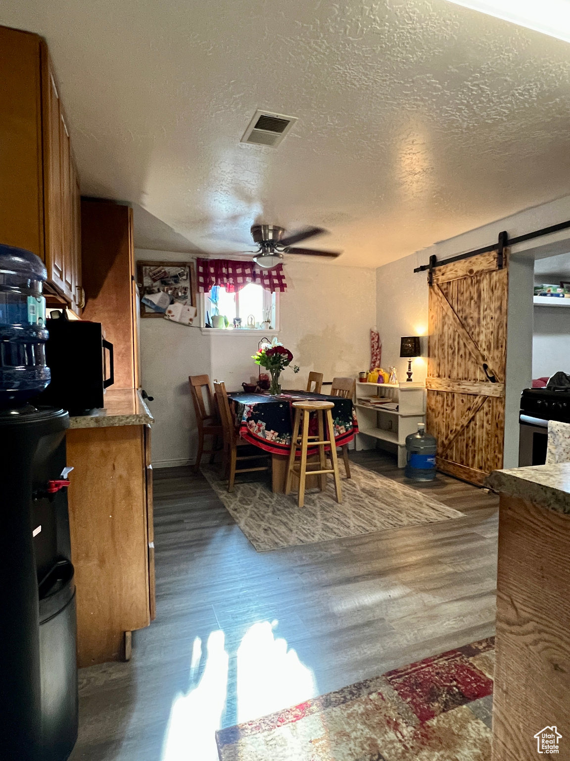 Dining room featuring ceiling fan, hardwood / wood-style floors, a barn door, and a textured ceiling