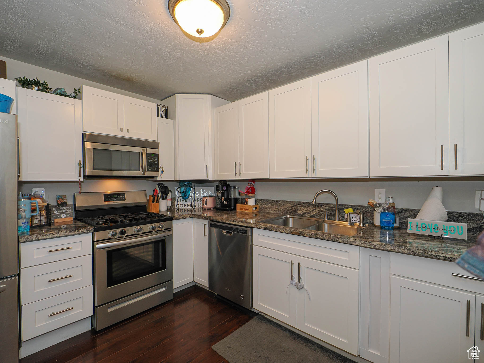 Kitchen with stainless steel appliances, a textured ceiling, white cabinets, and sink