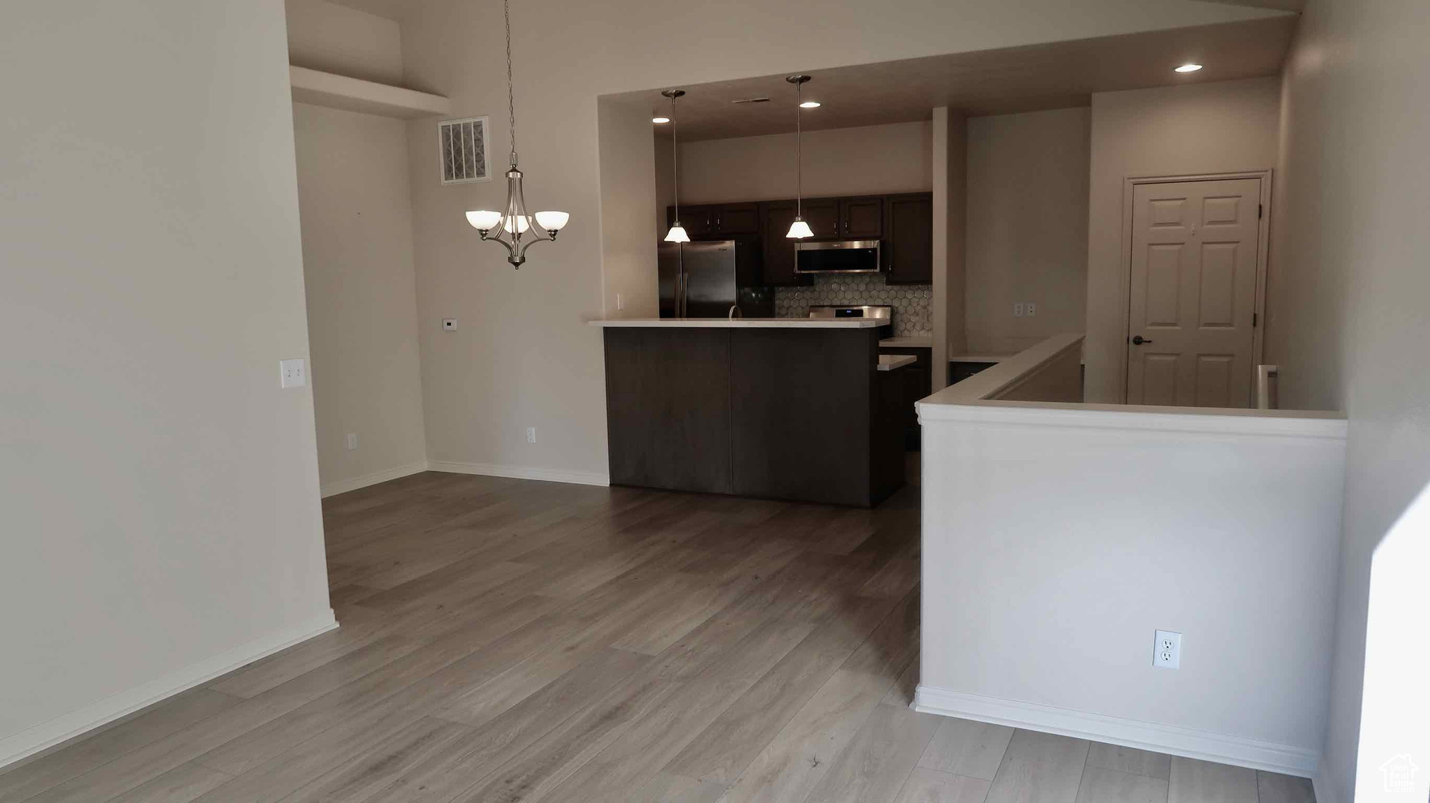 Kitchen with decorative backsplash, dark brown cabinets, stainless steel appliances, a notable chandelier, and hanging light fixtures