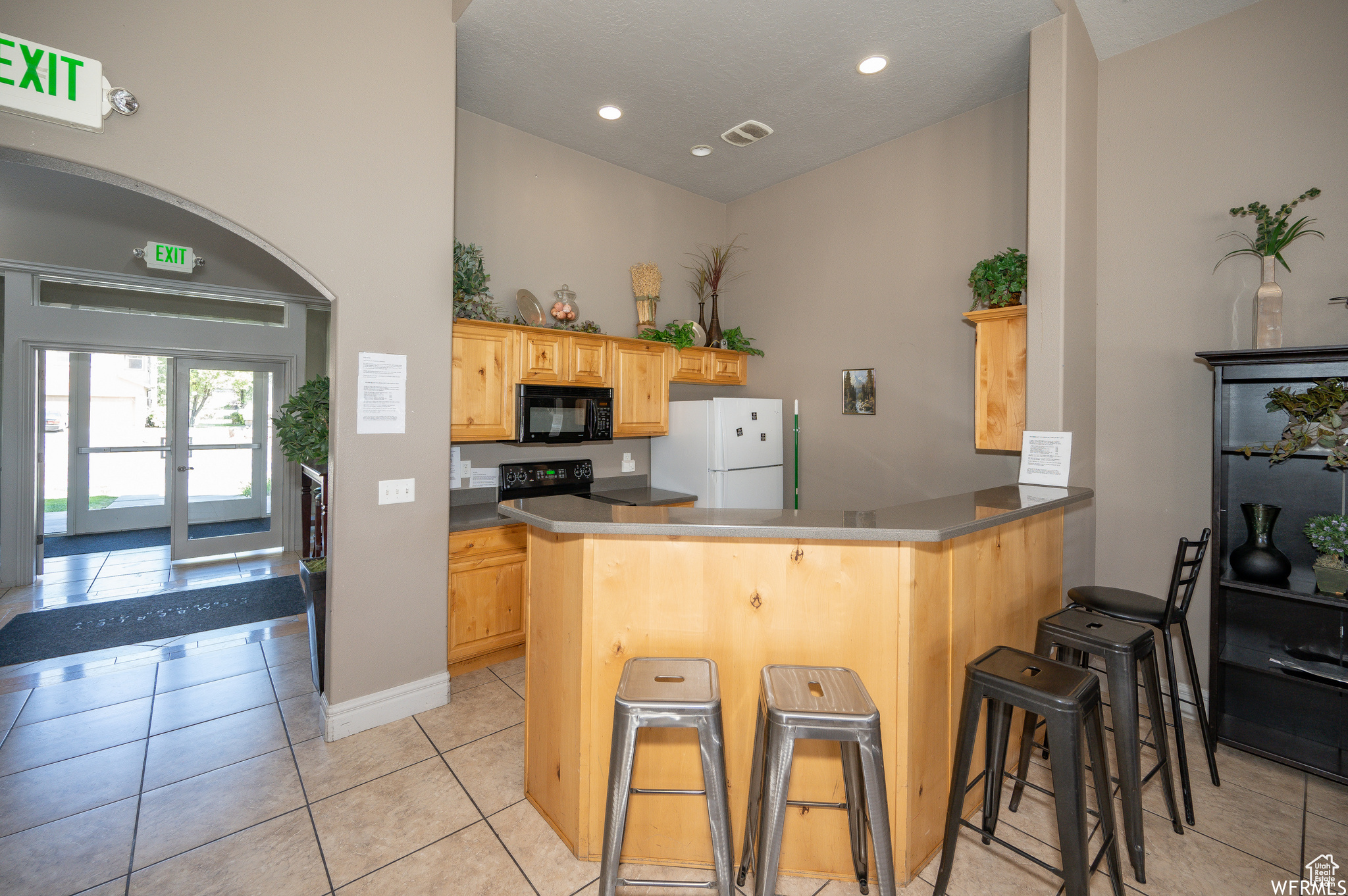 Kitchen featuring light brown cabinets, kitchen peninsula, a kitchen bar, light tile patterned floors, and black appliances