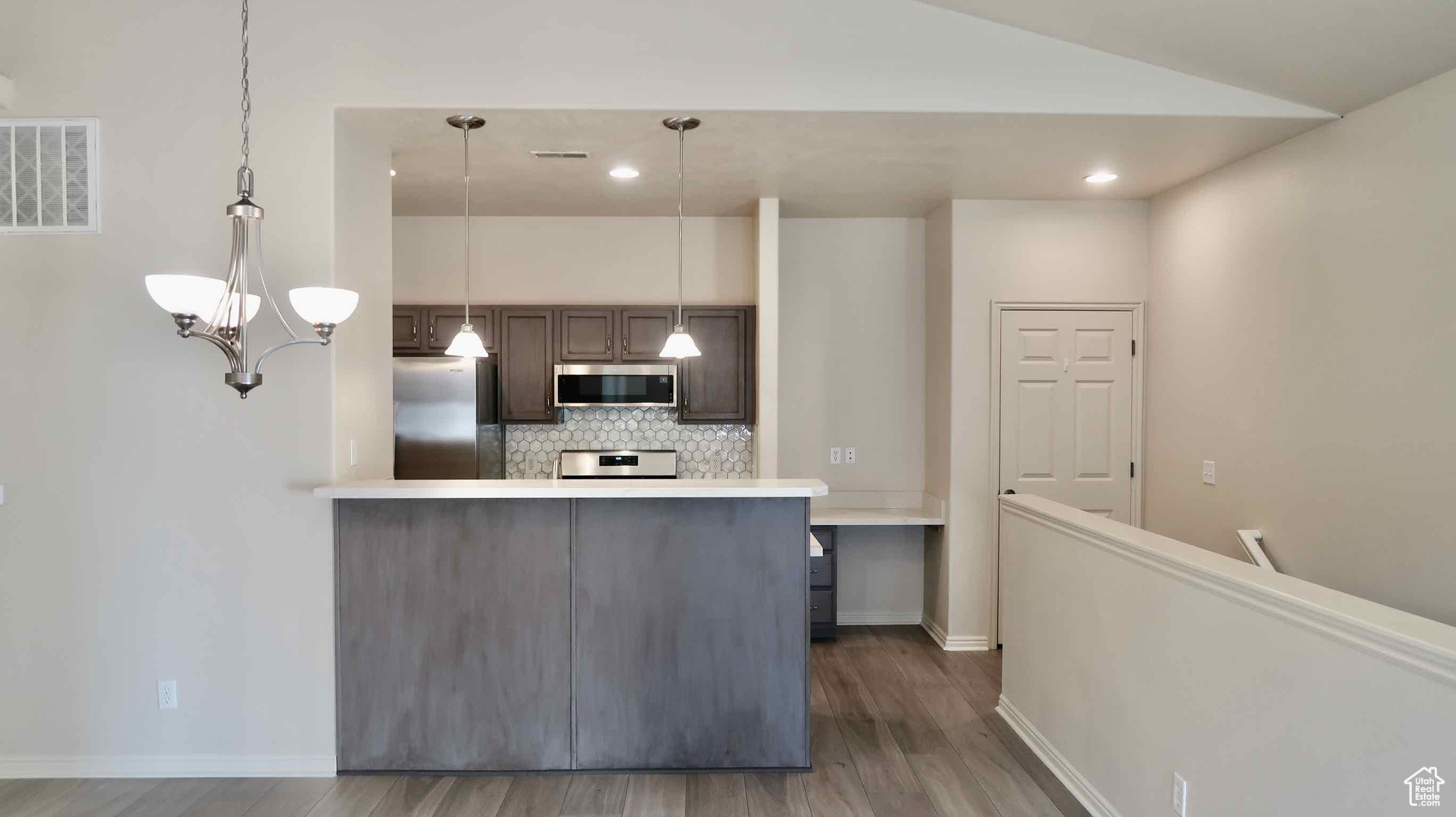 Kitchen with decorative backsplash, dark hardwood / wood-style flooring, hanging light fixtures, and appliances with stainless steel finishes