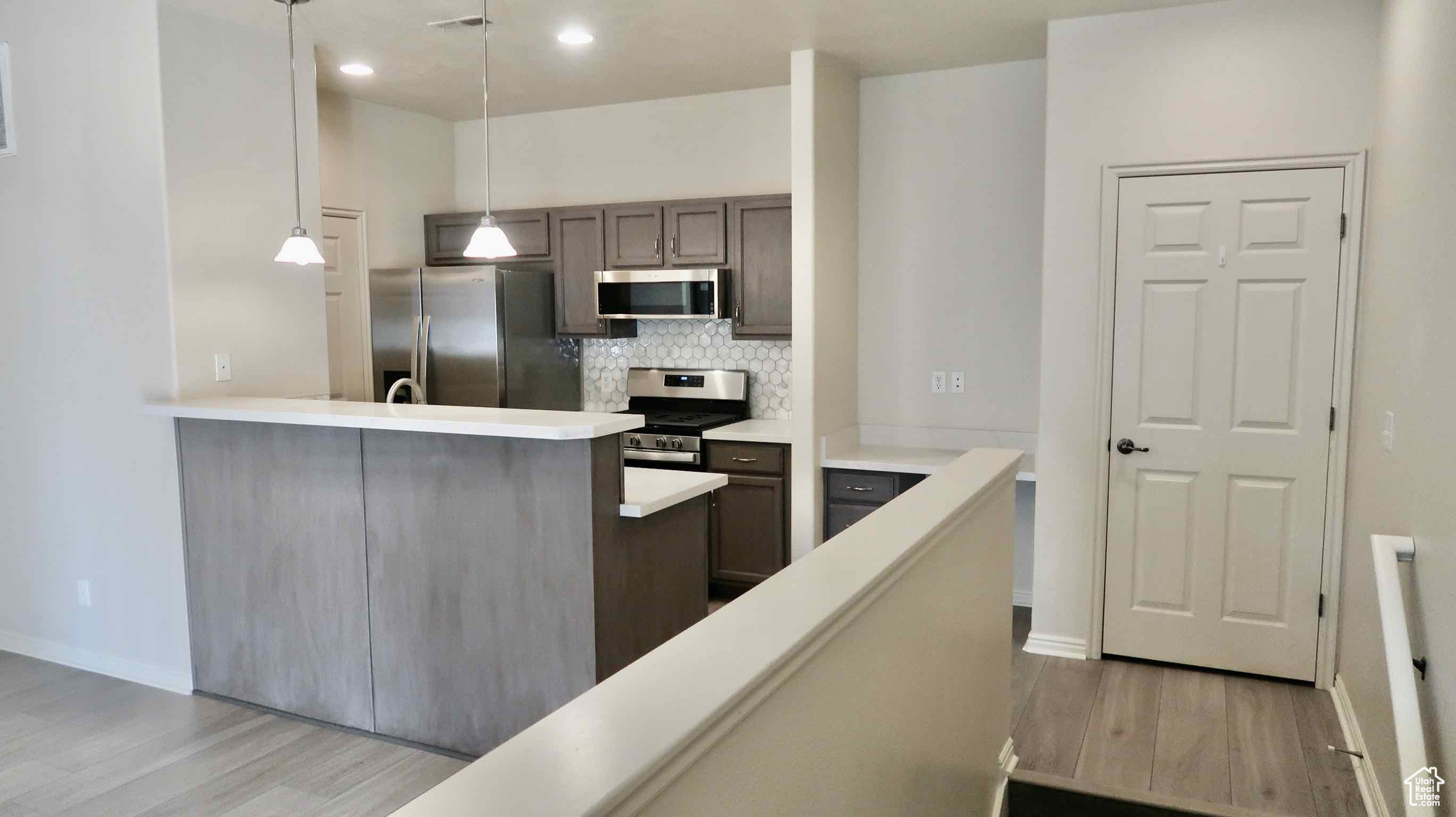 Kitchen with stainless steel appliances, tasteful backsplash, kitchen peninsula, decorative light fixtures, and light wood-type flooring