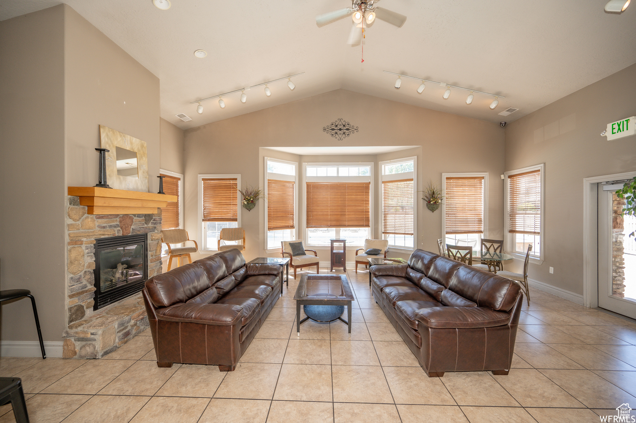 Living room featuring ceiling fan, a stone fireplace, a wealth of natural light, and light tile patterned flooring