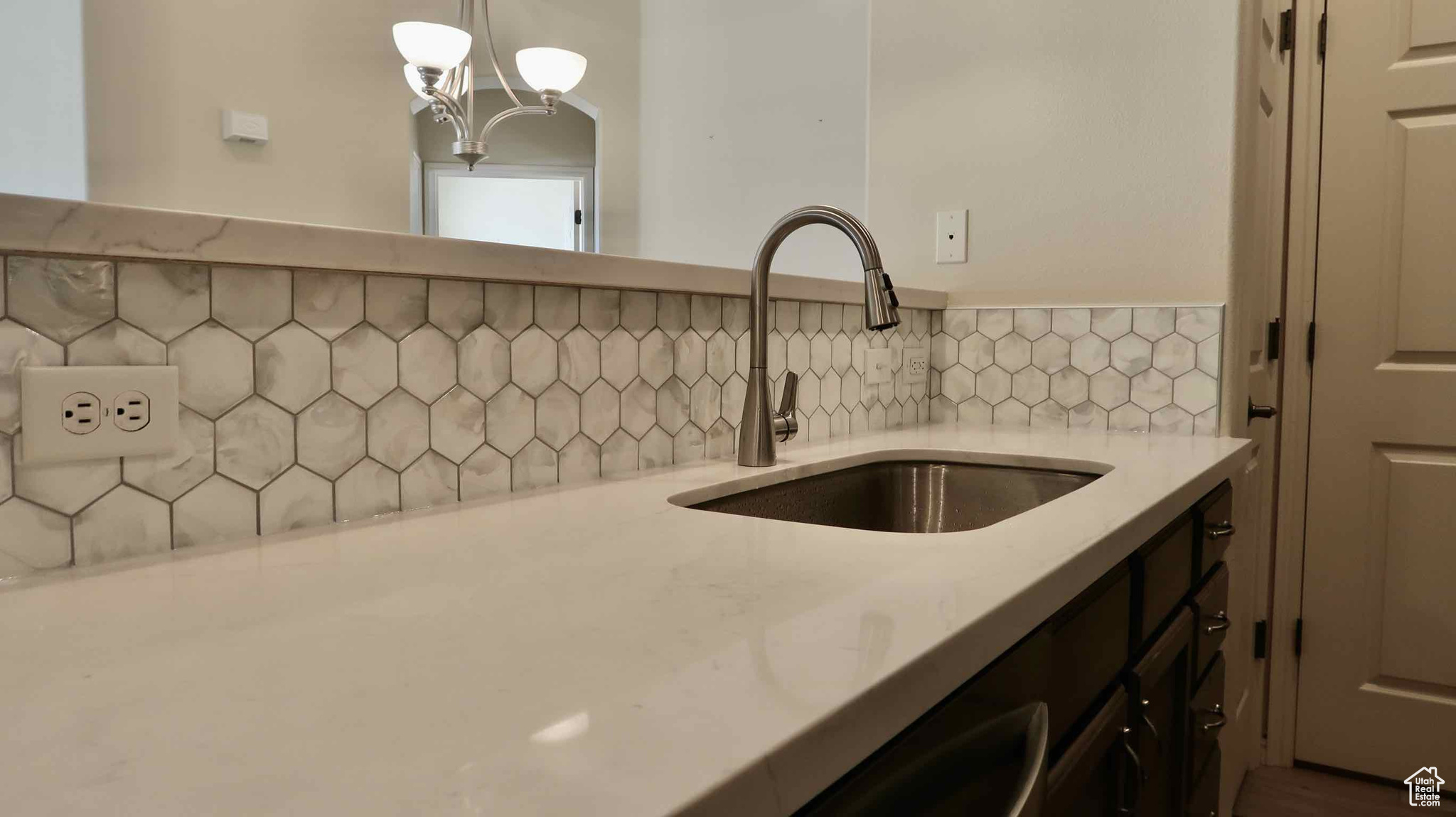 Kitchen with light stone countertops, sink, tasteful backsplash, a notable chandelier, and decorative light fixtures