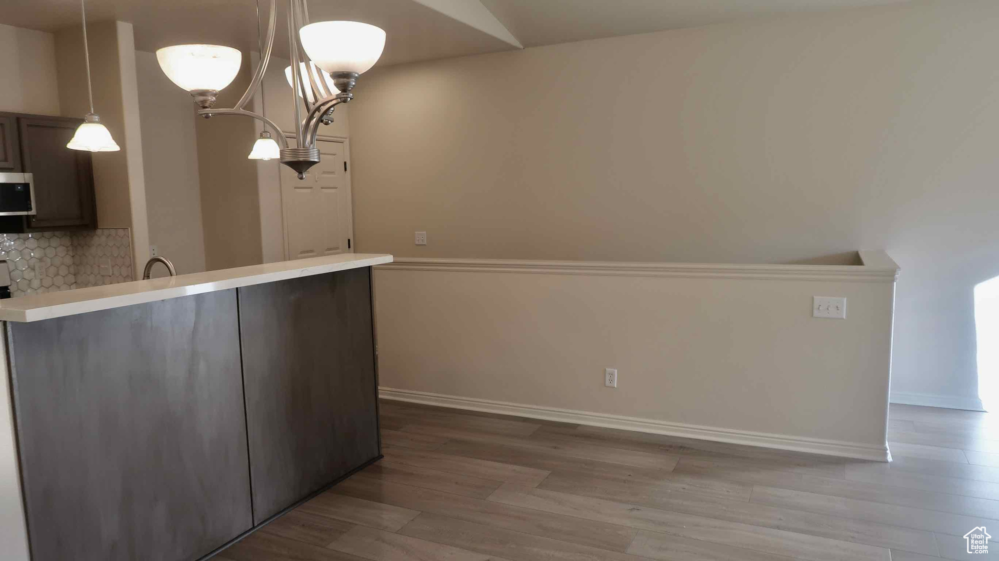 Kitchen with backsplash, kitchen peninsula, light wood-type flooring, decorative light fixtures, and dark brown cabinetry