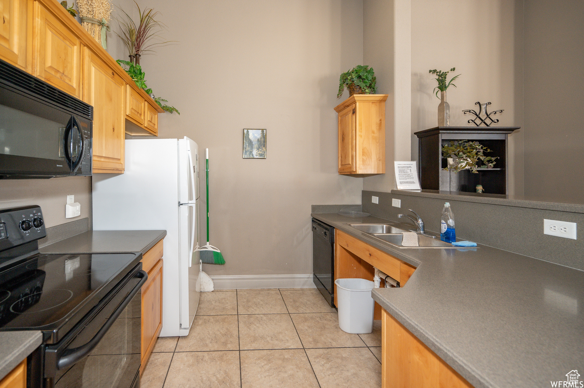 Kitchen with sink, light tile patterned flooring, black appliances, and light brown cabinets