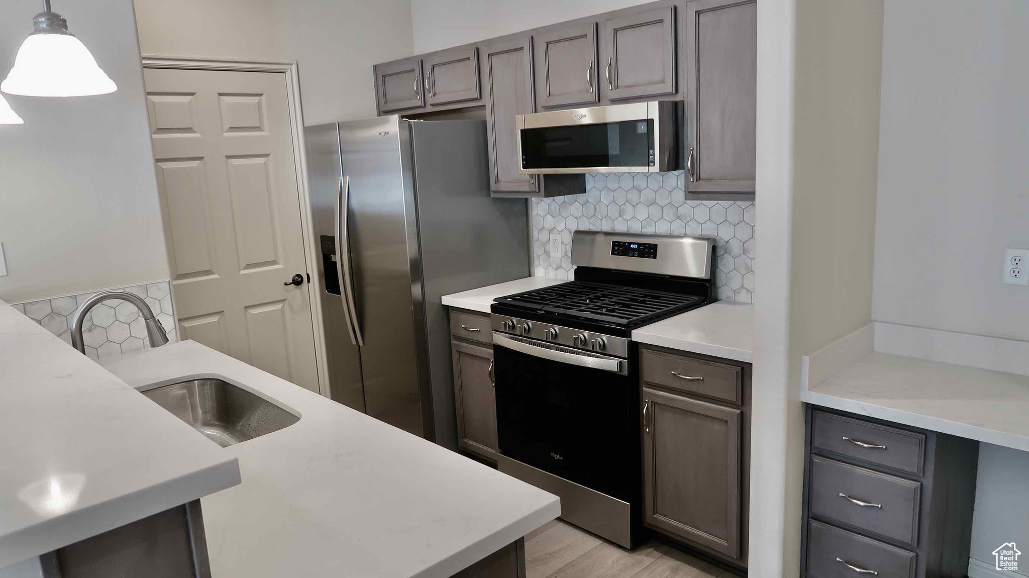 Kitchen featuring backsplash, stainless steel appliances, sink, pendant lighting, and light hardwood / wood-style flooring