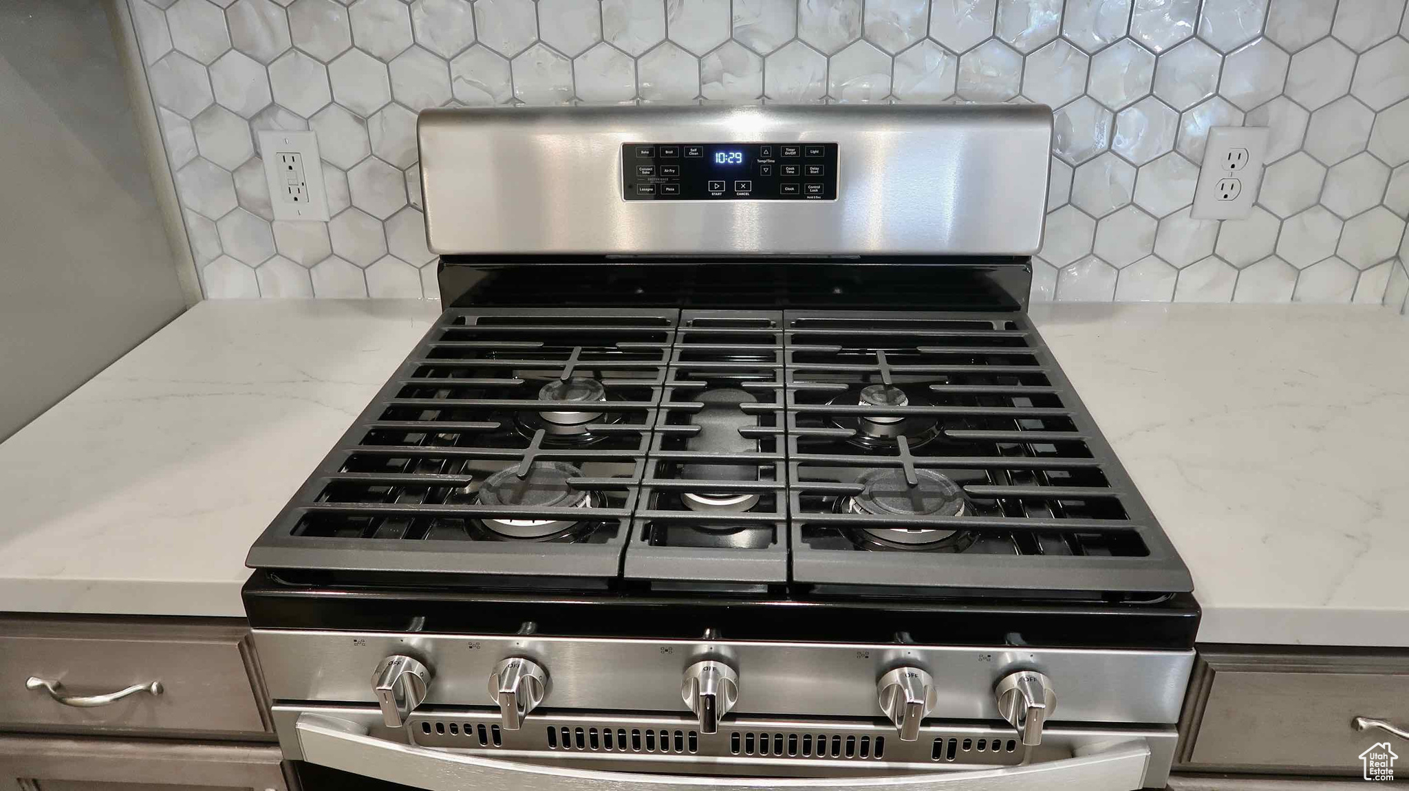 Details with light stone counters, backsplash, and stainless steel range with gas stovetop