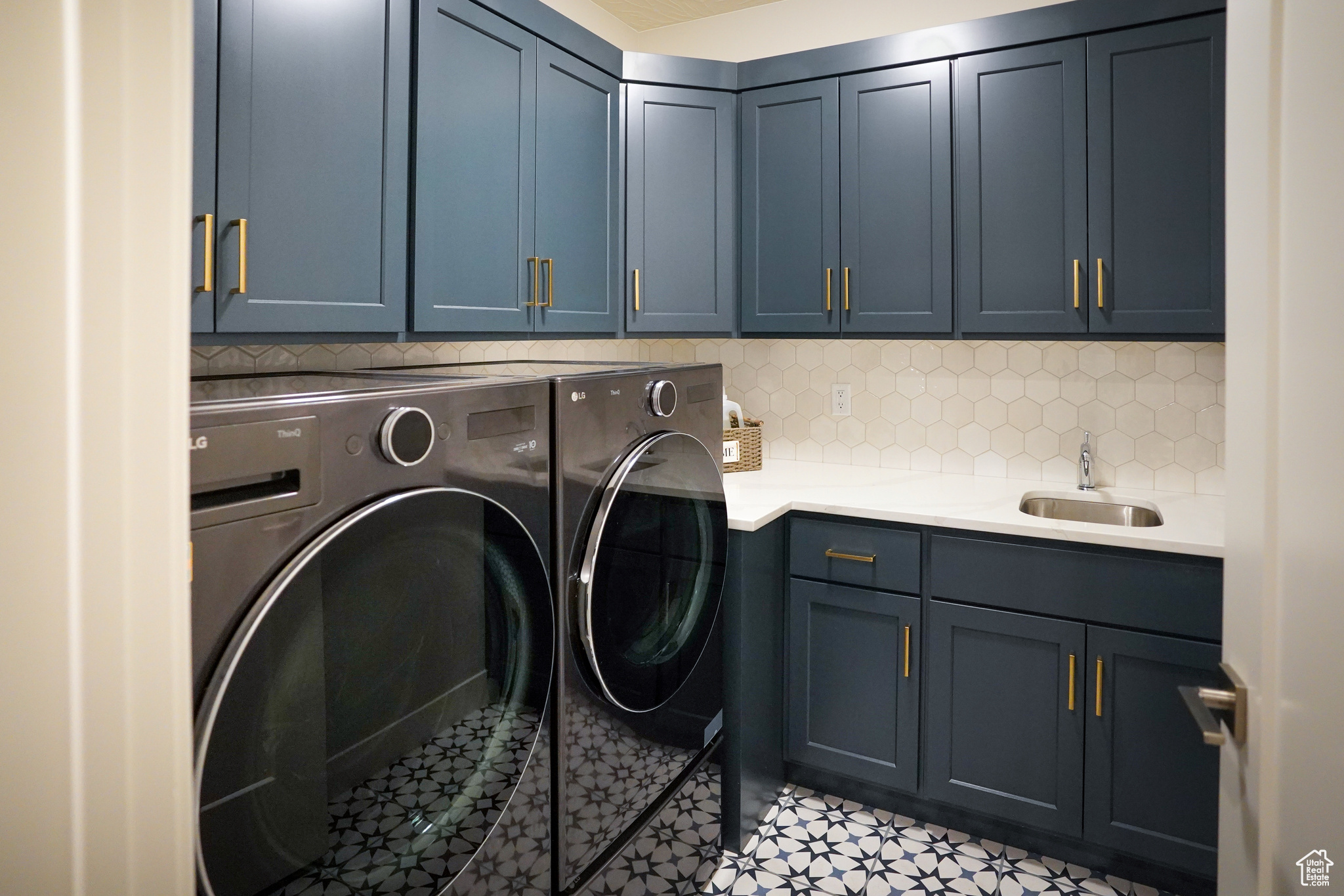 Laundry room with full upper and lower cabinets, including laundry sink and tiled backsplash.