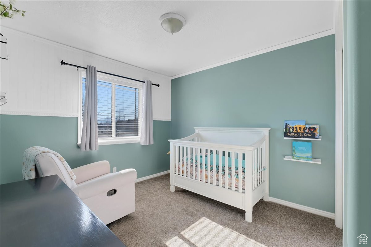 Bedroom featuring a nursery area, crown molding, and carpet flooring