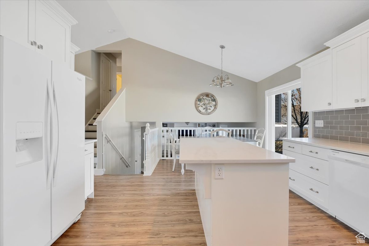 Kitchen with vaulted ceiling, a center island, decorative backsplash, white appliances, and white cabinetry