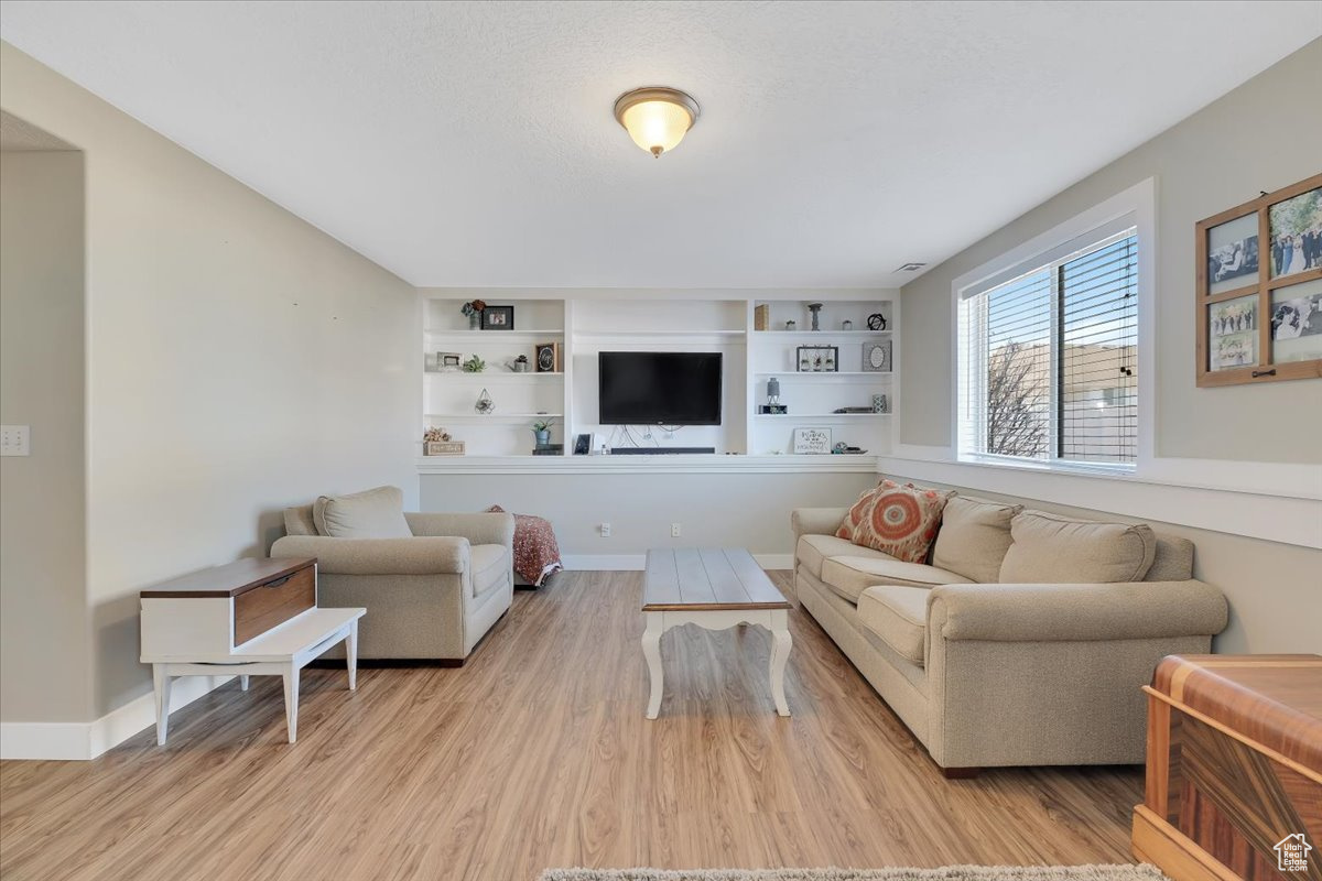 Living room with built in features and light hardwood / wood-style floors