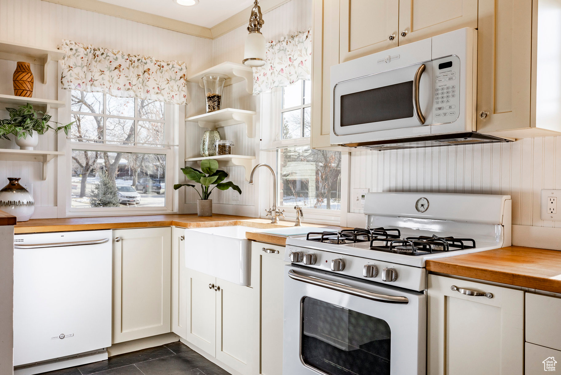 Kitchen featuring decorative light fixtures, white appliances, dark tile patterned floors, white cabinets, and butcher block counters