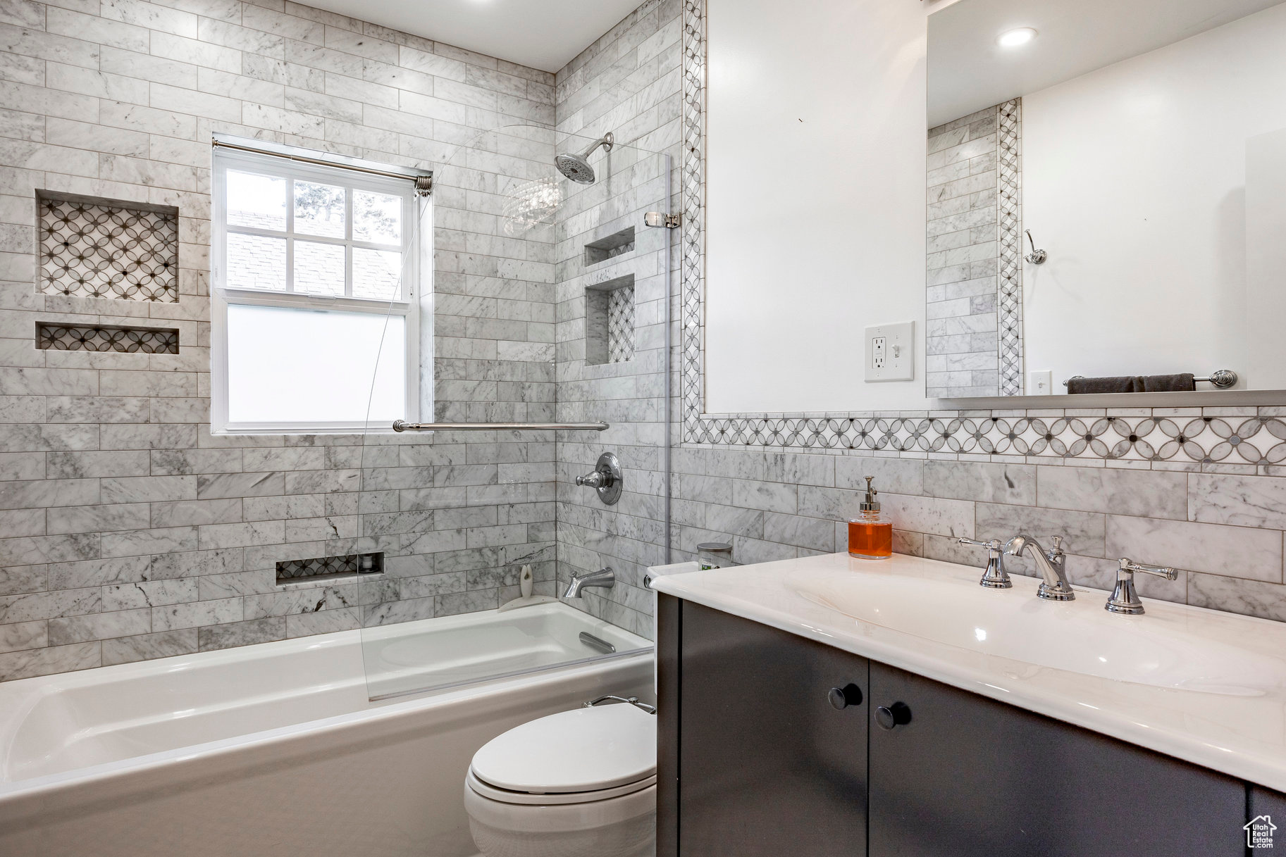 Full bathroom with tile walls, toilet, vanity, and tiled shower / bath