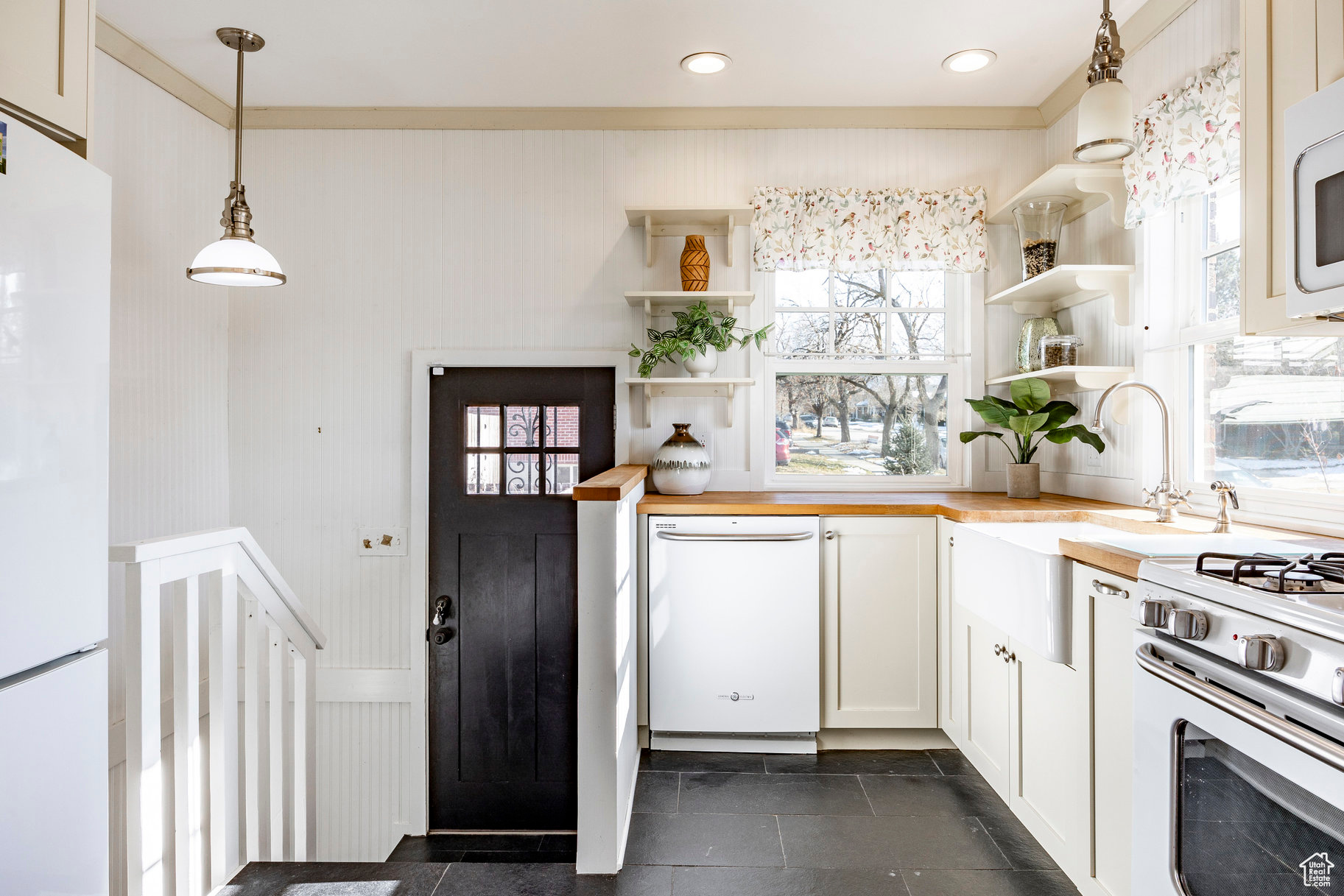 Kitchen featuring pendant lighting, butcher block countertops, sink, white appliances, and white cabinetry