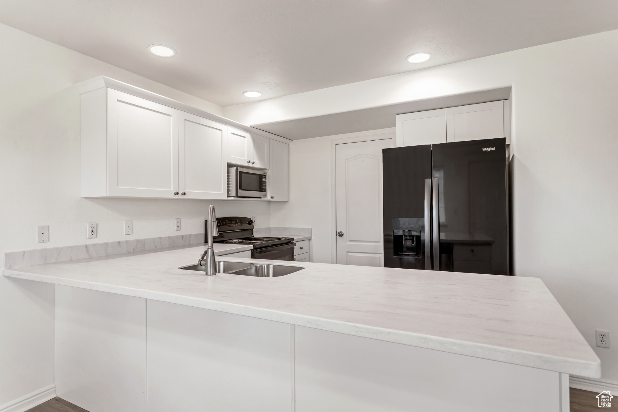 Kitchen with sink, white cabinets, black appliances, and kitchen peninsula