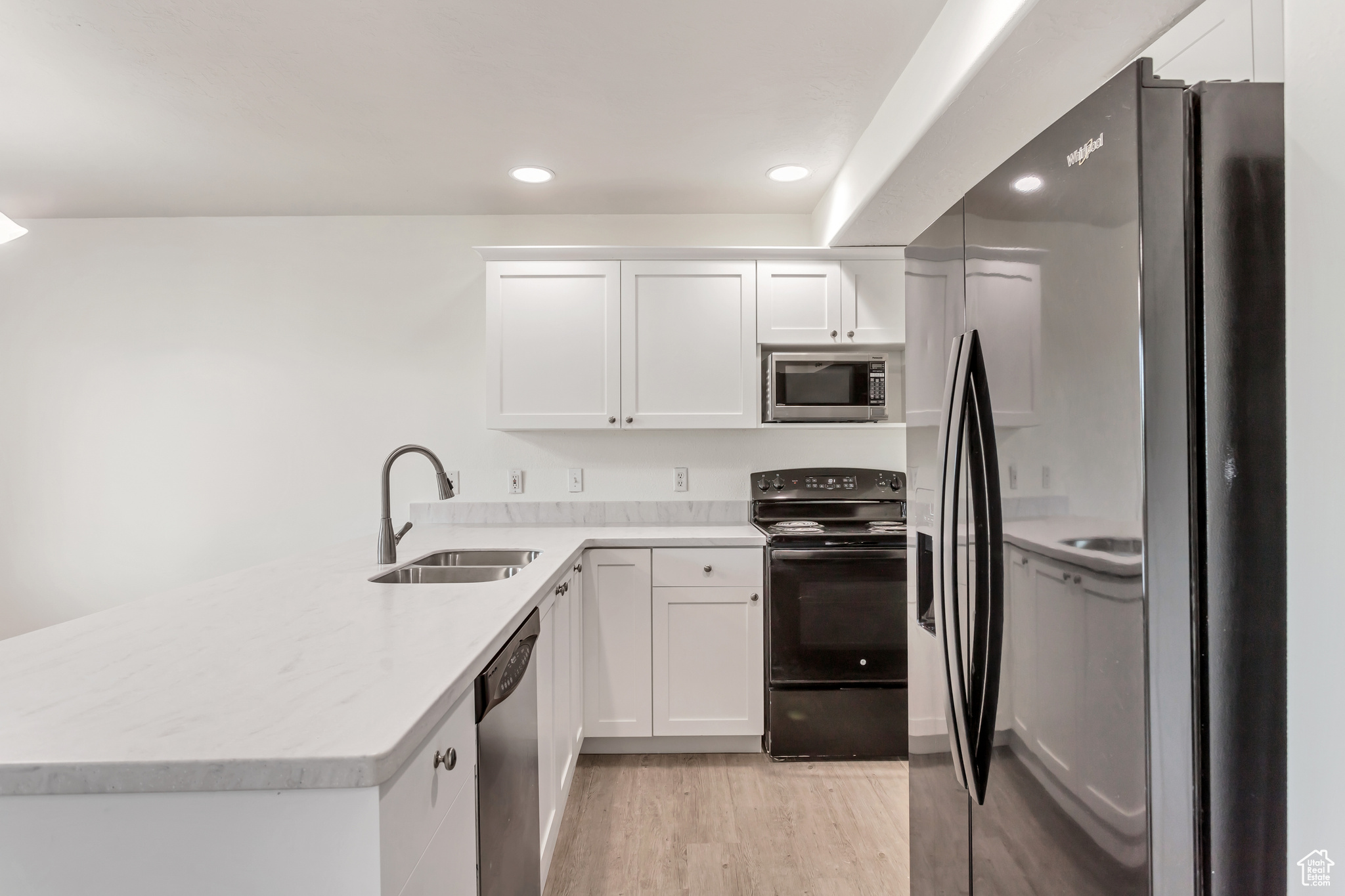 Kitchen with black appliances, white cabinets, kitchen peninsula, and sink