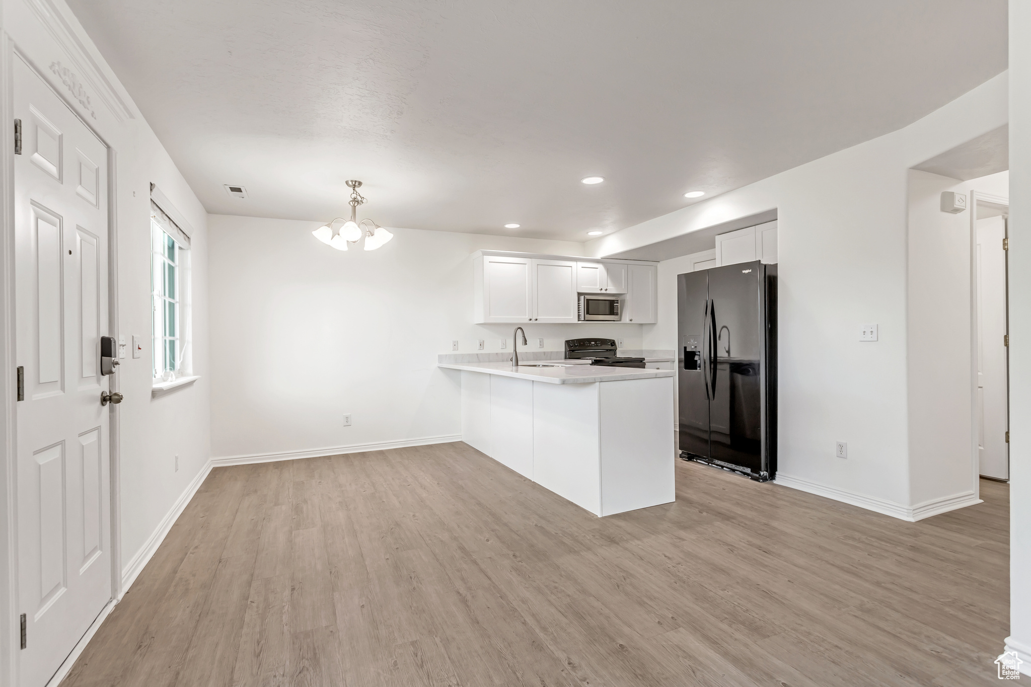 Kitchen with black appliances, kitchen peninsula, sink, an inviting chandelier, and white cabinets