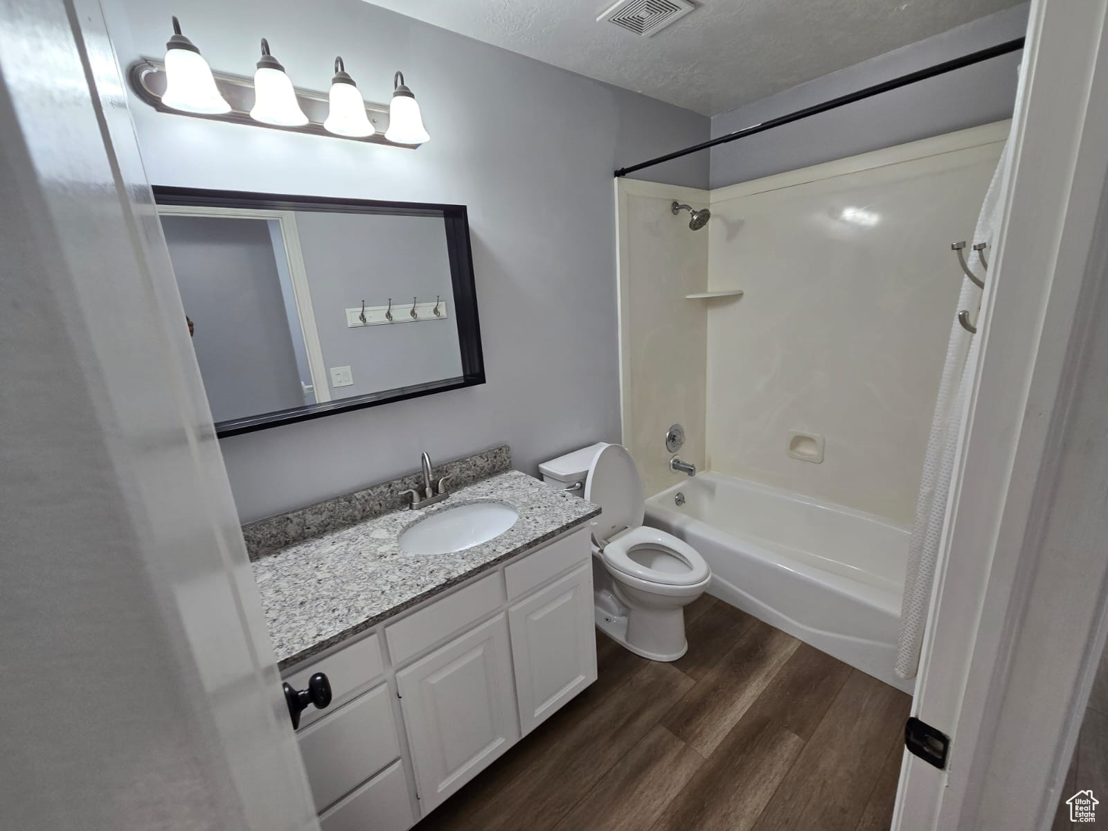 Full bathroom with a textured ceiling, shower / bathtub combination, vanity, toilet, and hardwood / wood-style flooring