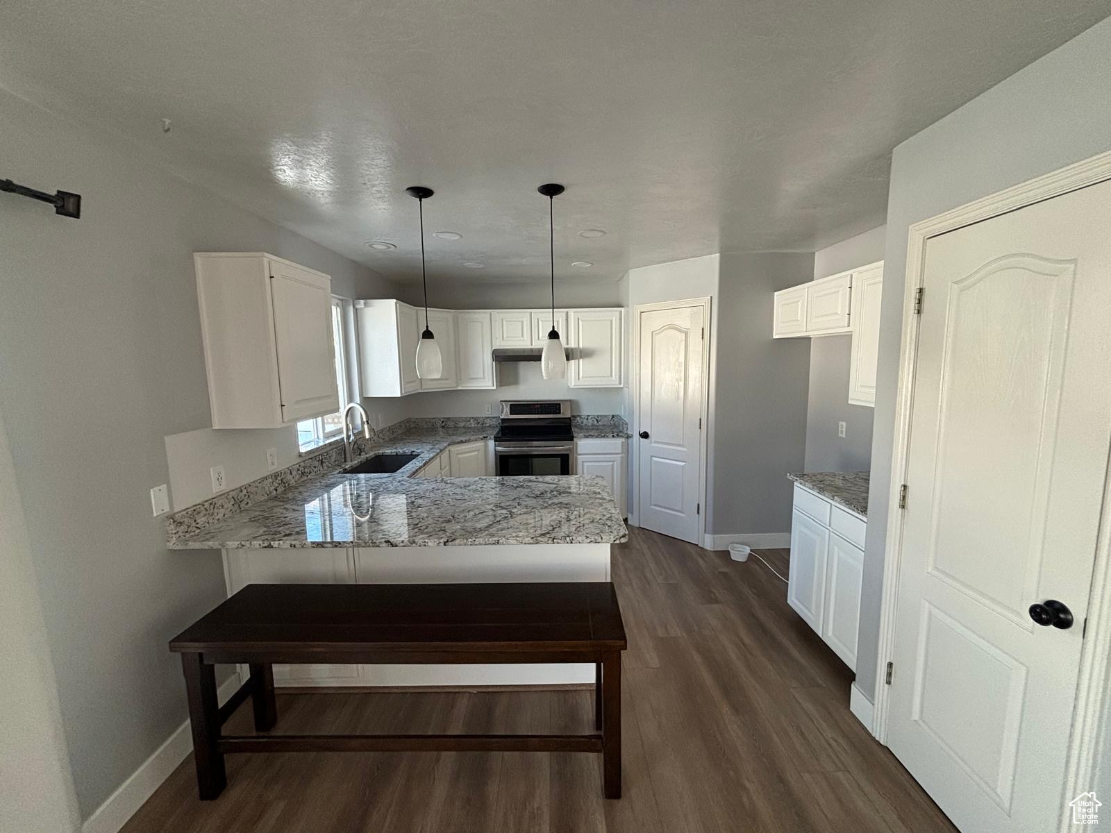 Kitchen with kitchen peninsula, hanging light fixtures, stainless steel range with electric cooktop, white cabinets, and dark hardwood / wood-style flooring