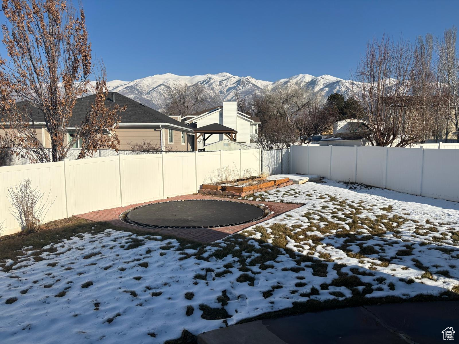 Yard layered in snow featuring a trampoline and a mountain view