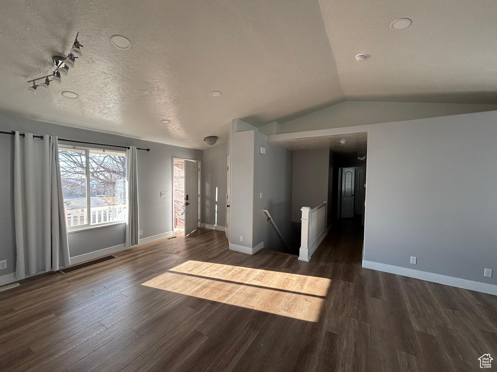 Living room with vaulted ceiling, dark wood-type flooring, track lighting, and a textured ceiling