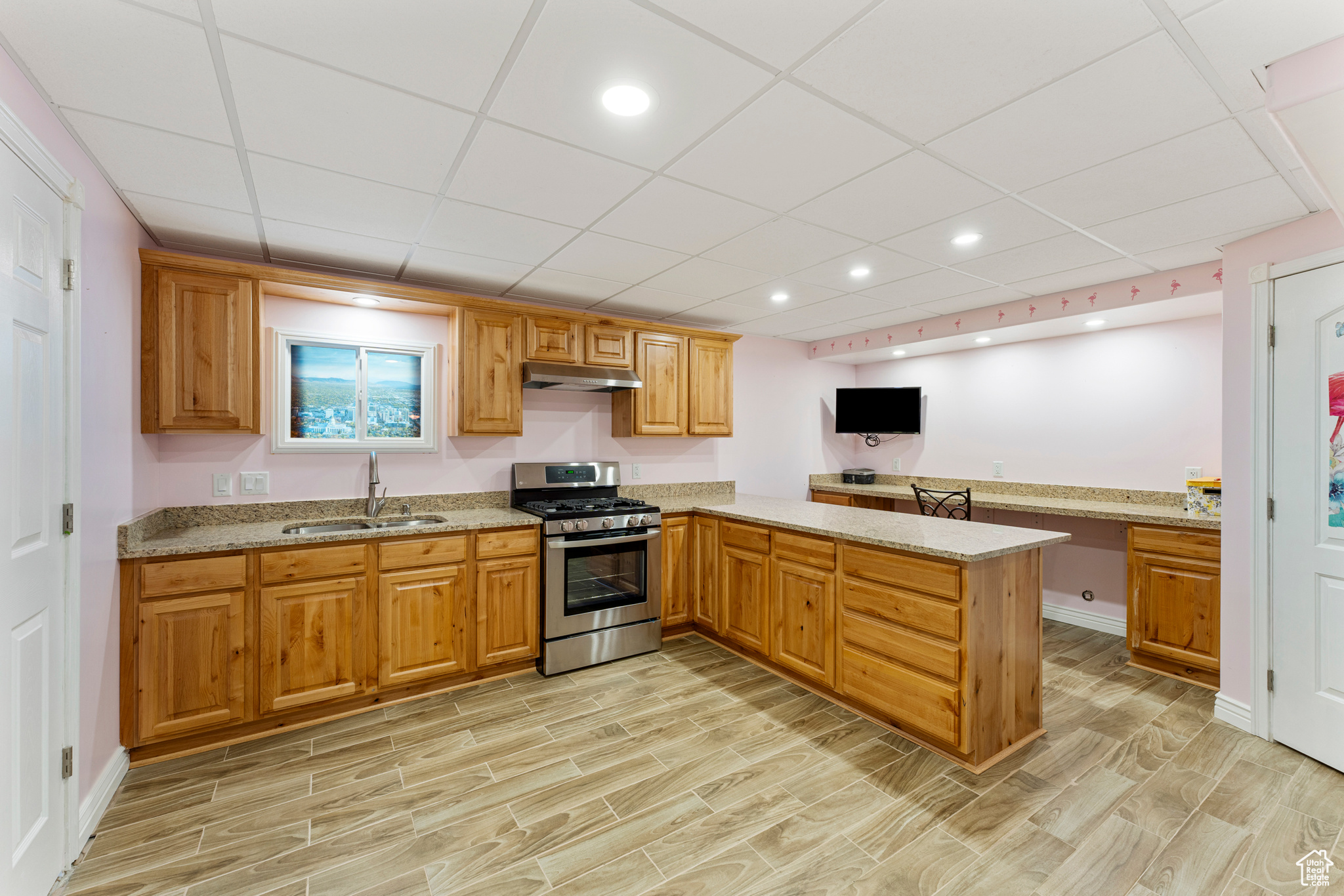 Kitchen with sink, light stone counters, kitchen peninsula, stainless steel range with gas stovetop, and a drop ceiling