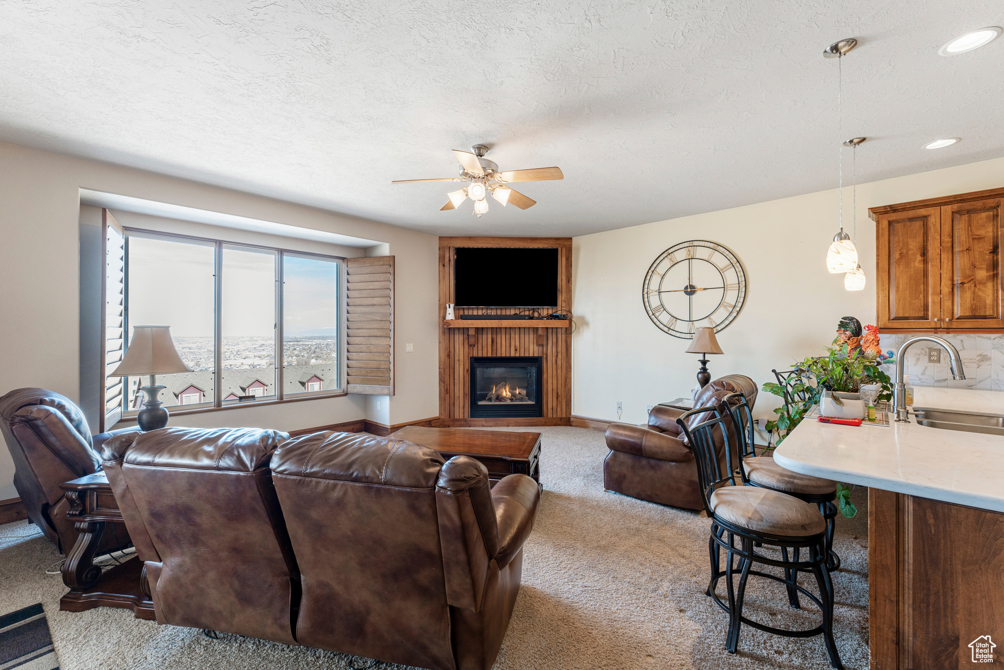 Carpeted living room with ceiling fan, sink, a textured ceiling, and a fireplace