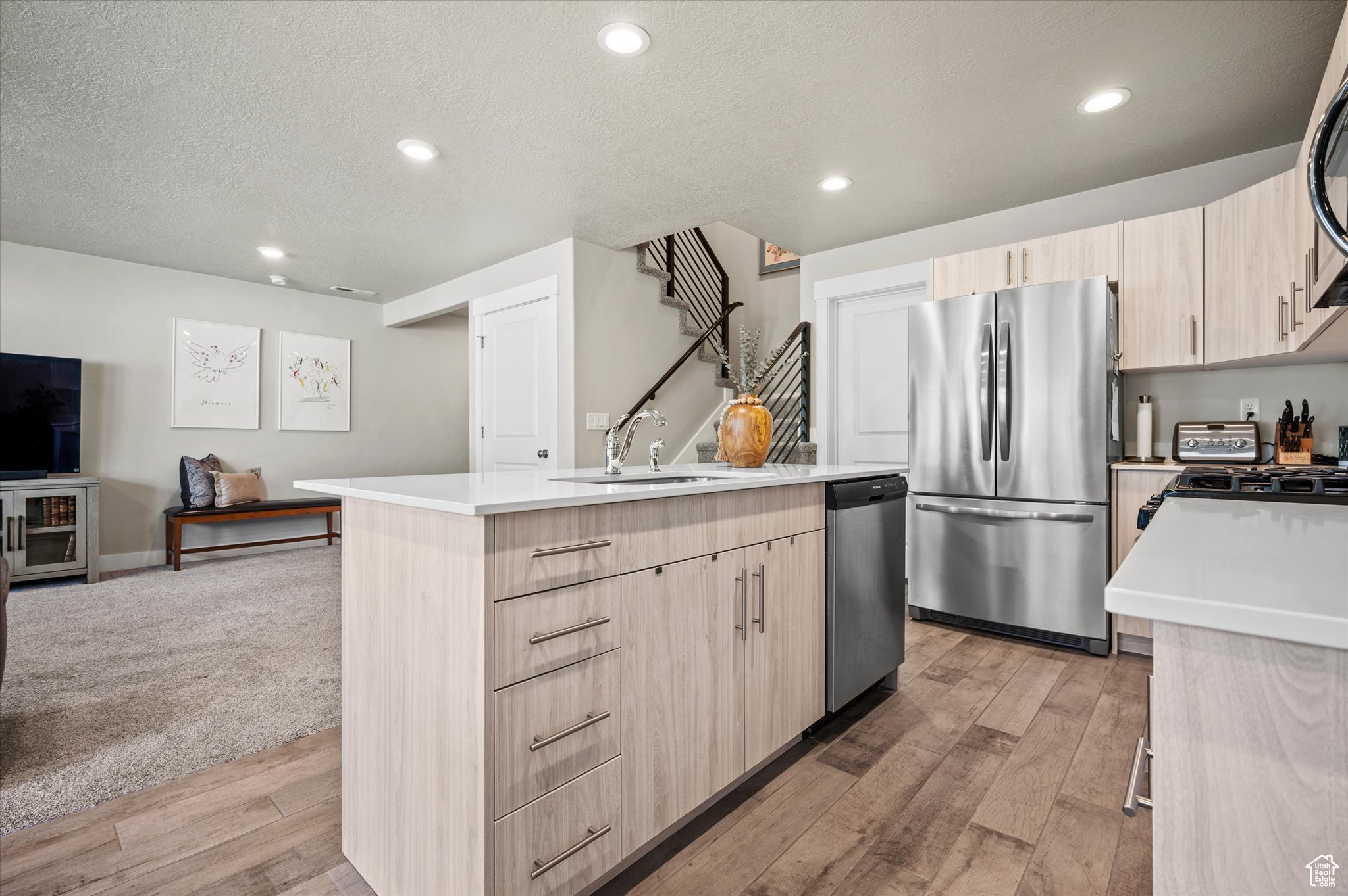 Kitchen with appliances with stainless steel finishes, light brown cabinets, a kitchen island with sink, light wood-type flooring, and sink