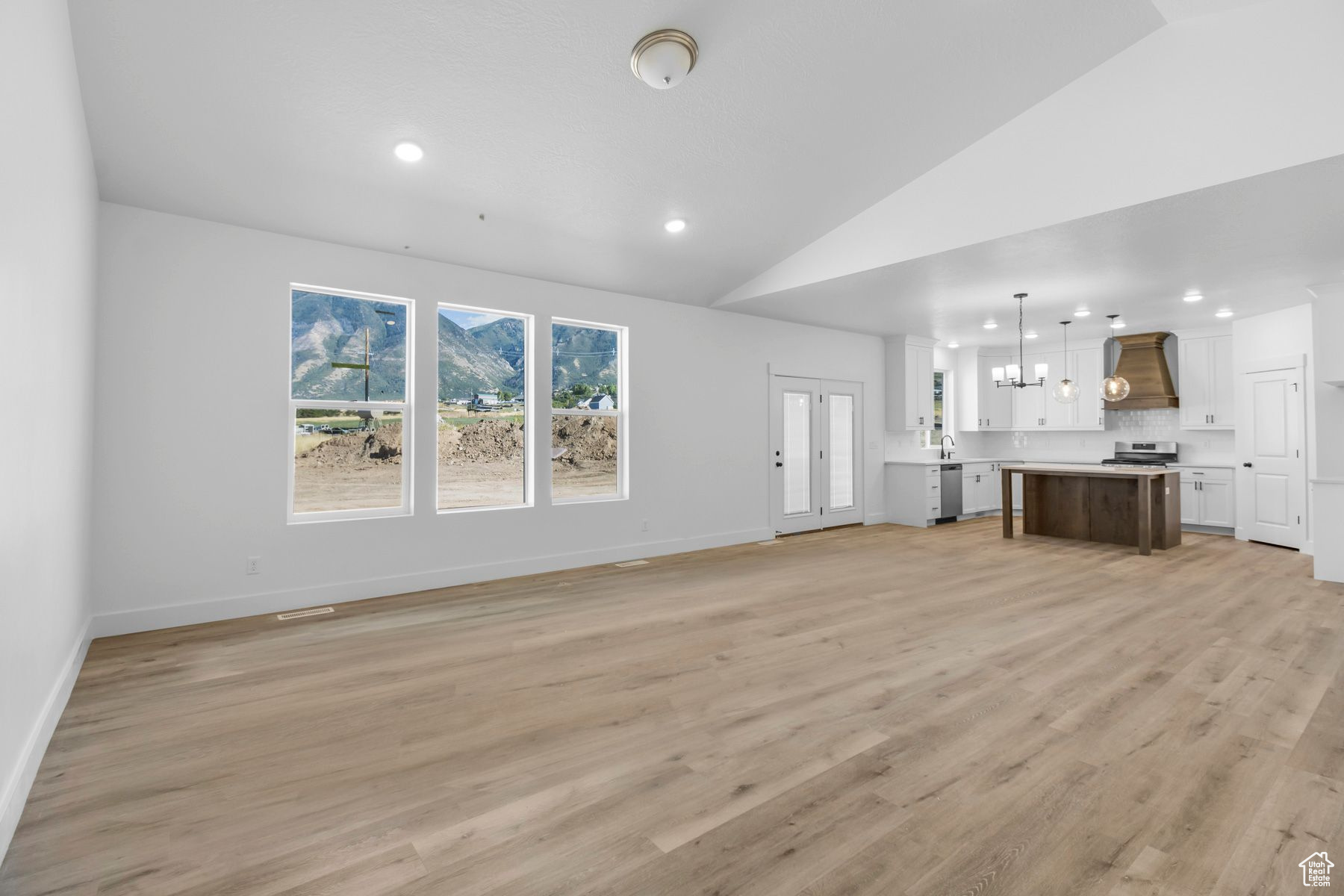 Unfurnished living room featuring vaulted ceiling, a notable chandelier, sink, and light hardwood / wood-style floors