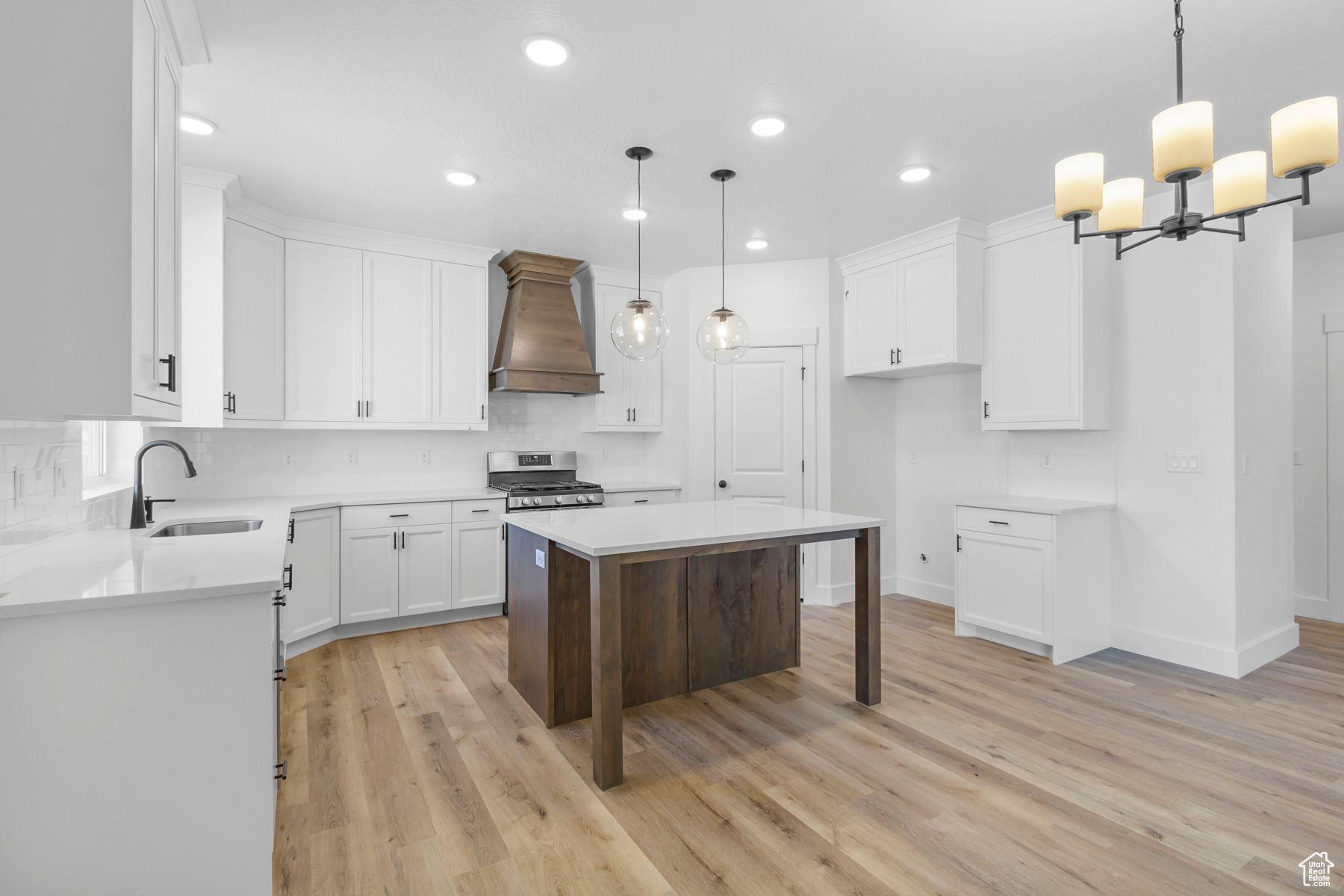 Kitchen featuring stainless steel range oven, white cabinetry, sink, hanging light fixtures, and custom range hood