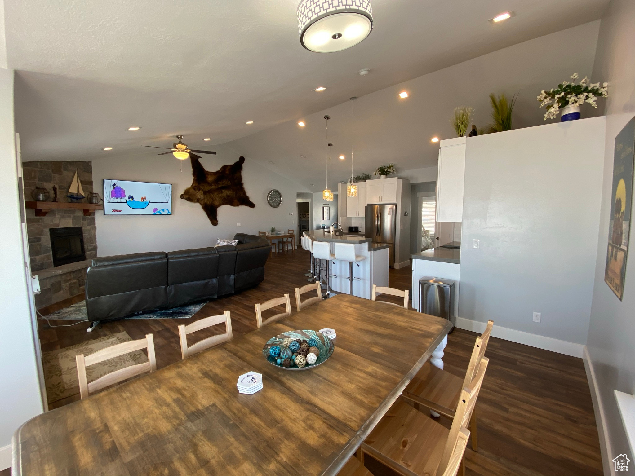 Dining room featuring ceiling fan, vaulted ceiling, dark hardwood / wood-style flooring, and a stone fireplace