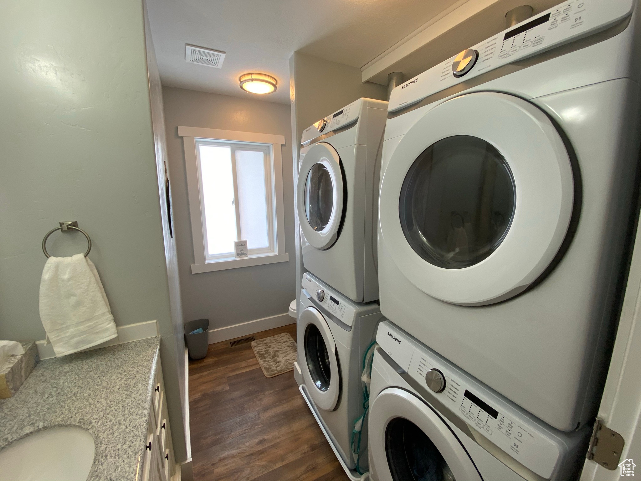 Laundry room with stacked washer / drying machine, dark hardwood / wood-style floors, and sink