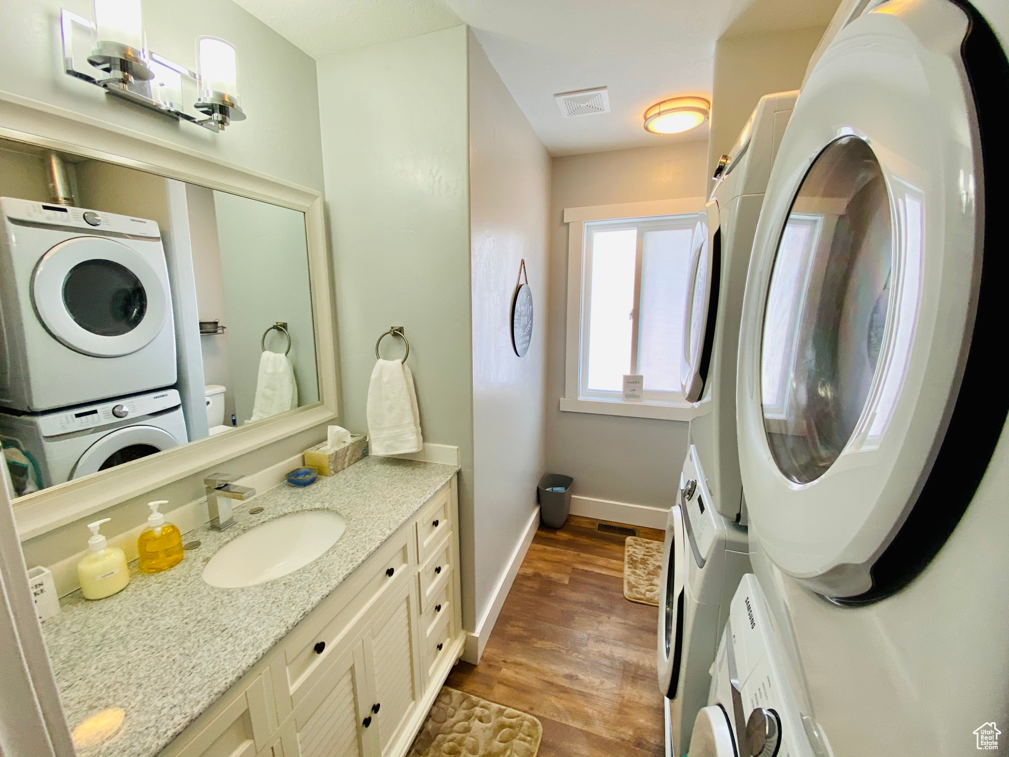 Bathroom featuring stacked washing maching and dryer, toilet, hardwood / wood-style floors, and vanity