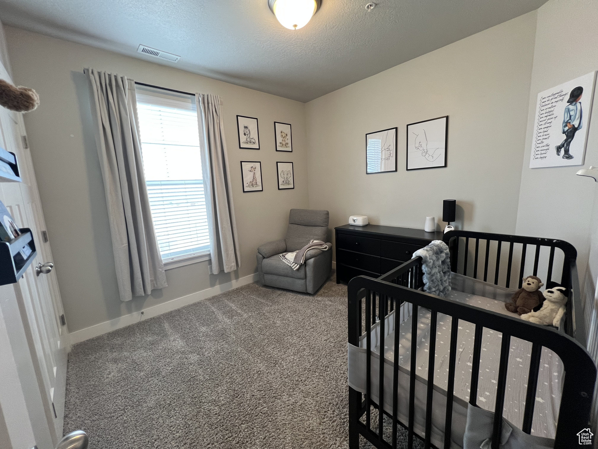 Bedroom featuring carpet floors, a nursery area, a textured ceiling, and multiple windows