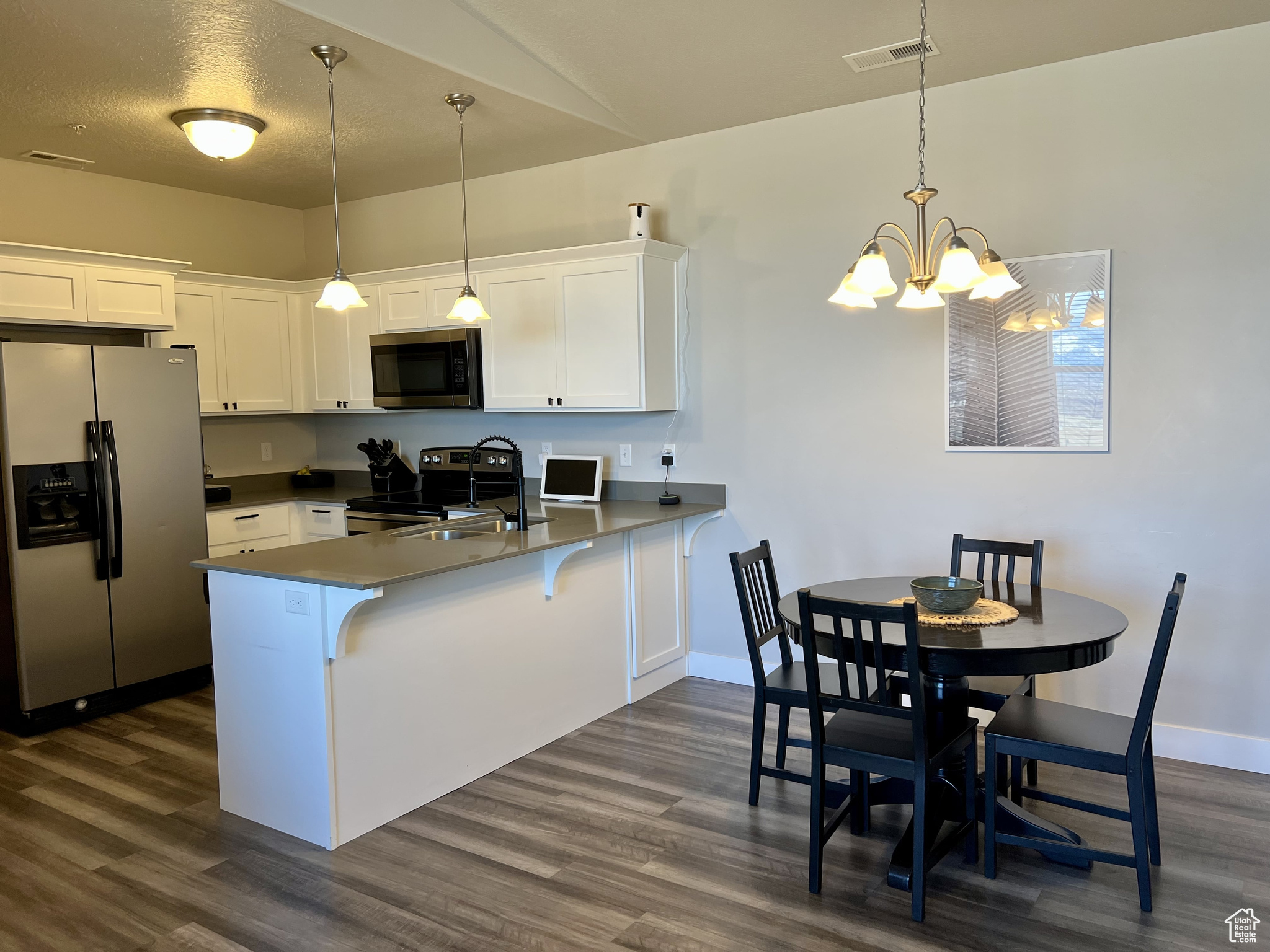 Kitchen with white cabinetry, kitchen peninsula, stainless steel appliances, decorative light fixtures, and a chandelier