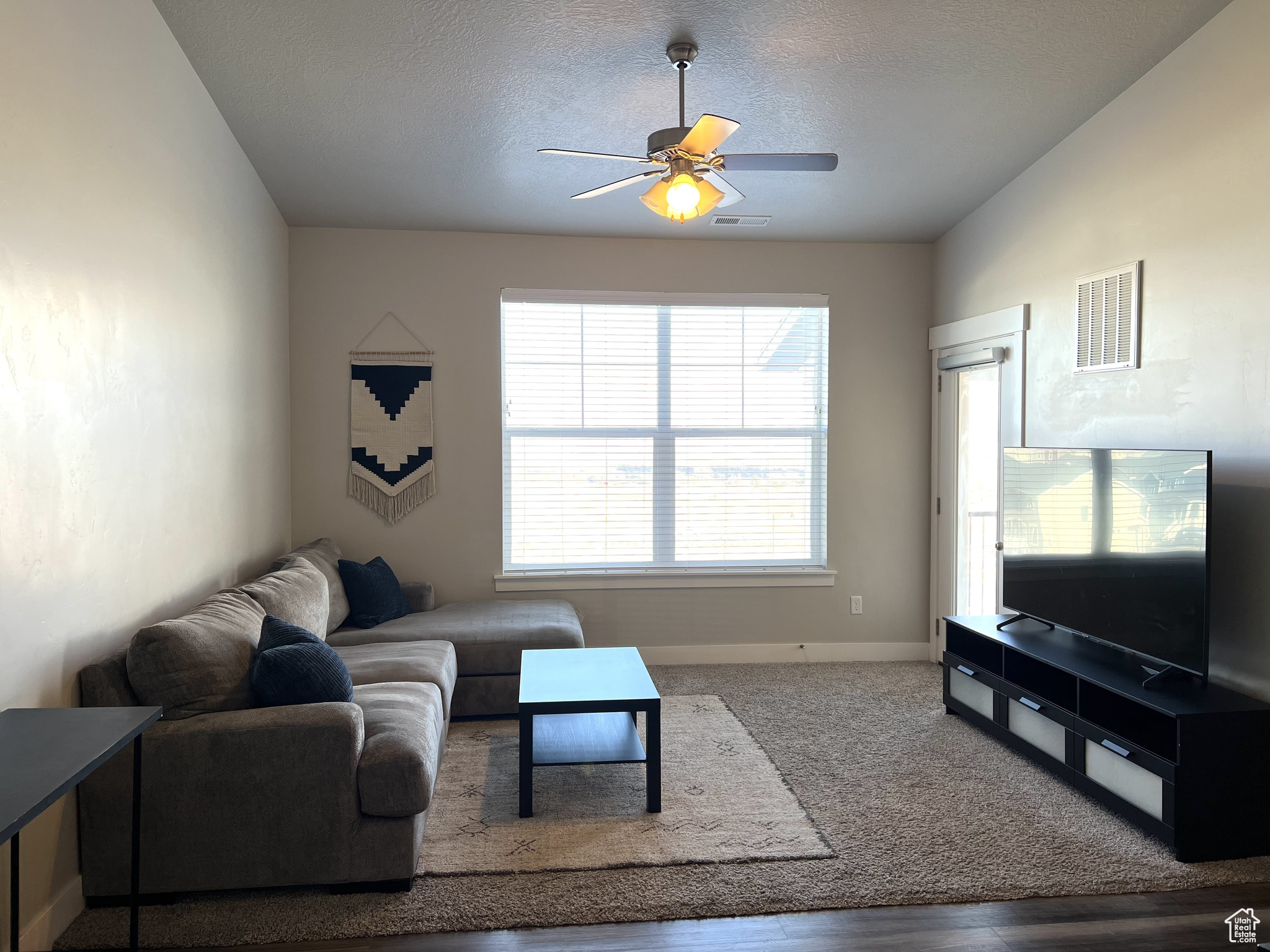 Living room featuring ceiling fan, a textured ceiling, and wood-type flooring