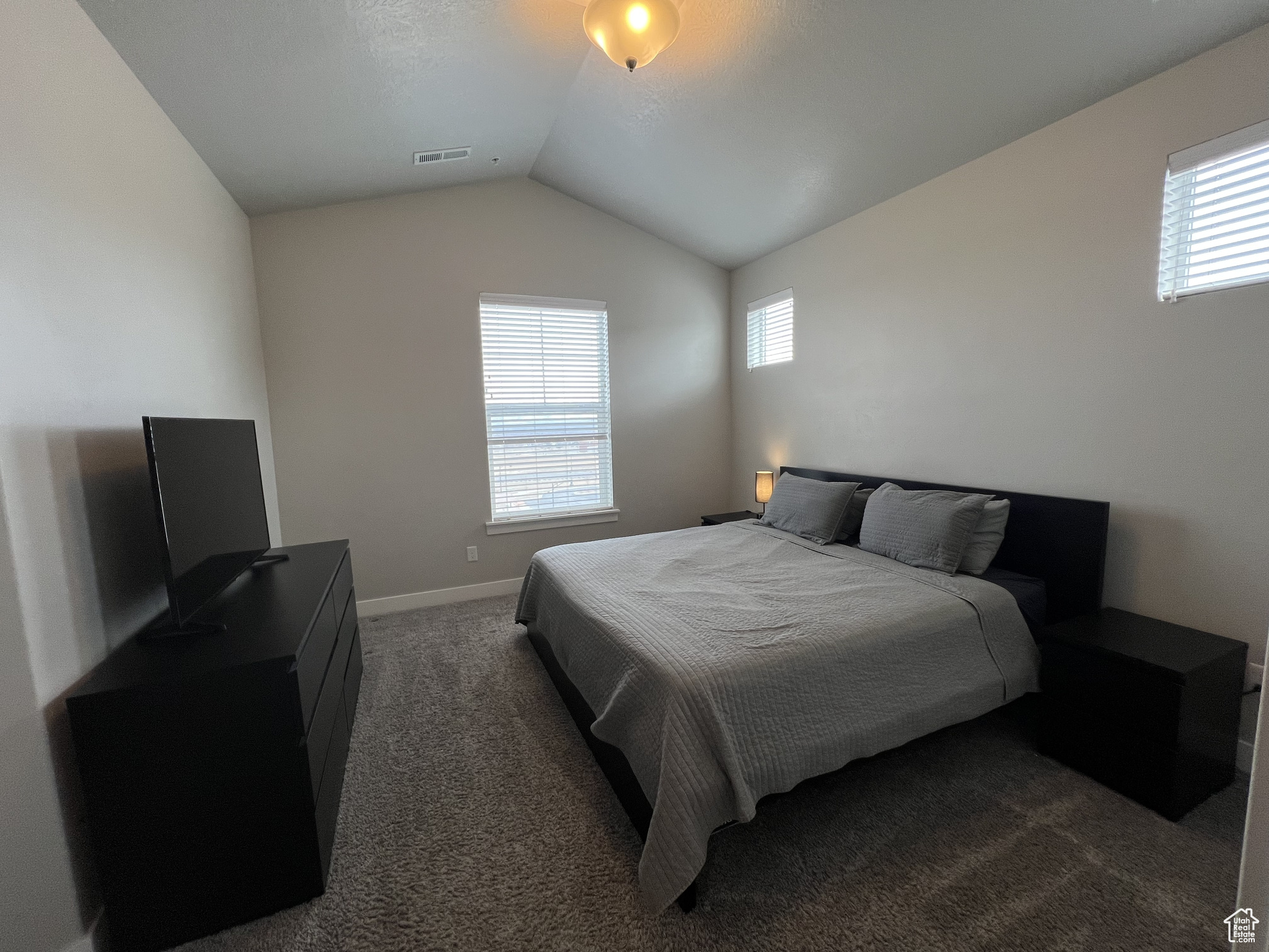 Bedroom with lofted ceiling, dark carpet, and multiple windows