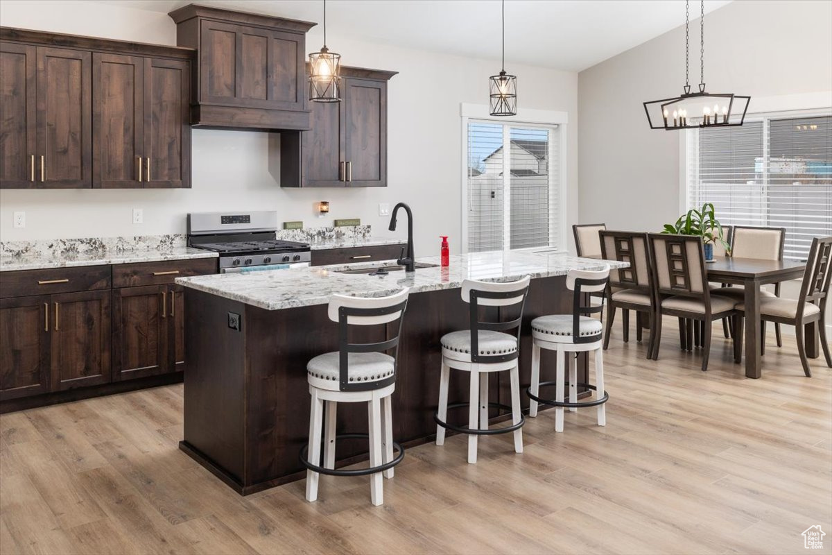 Kitchen with stainless steel gas range, light hardwood / wood-style flooring, a center island with sink, and sink