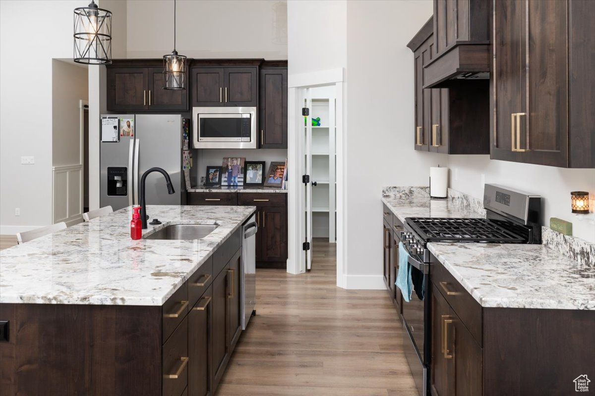 Kitchen with stainless steel appliances, a kitchen island with sink, dark brown cabinetry, and sink