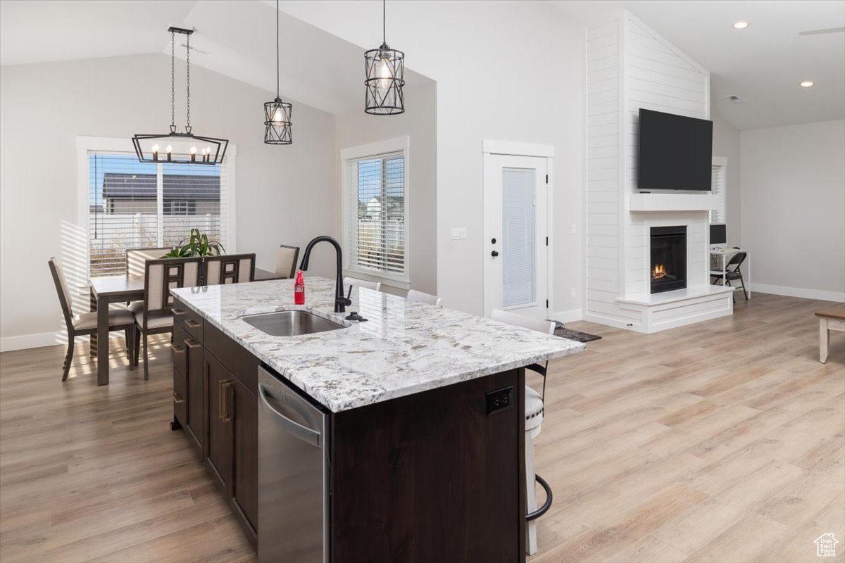 Kitchen with dishwasher, a fireplace, an island with sink, sink, and hanging light fixtures