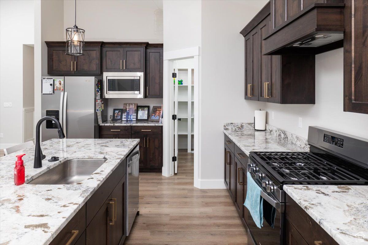 Kitchen with custom exhaust hood, stainless steel appliances, dark brown cabinets, pendant lighting, and sink