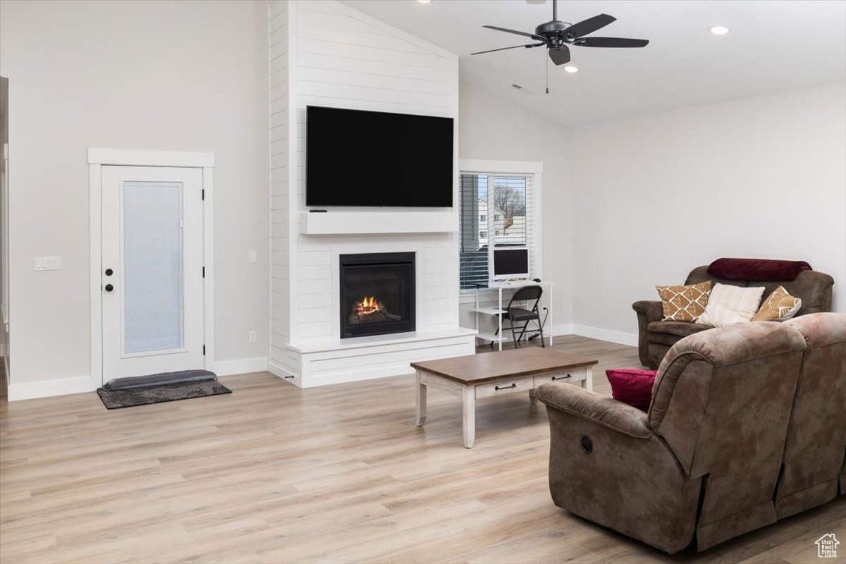 Living room featuring ceiling fan, high vaulted ceiling, a fireplace, and light hardwood / wood-style floors