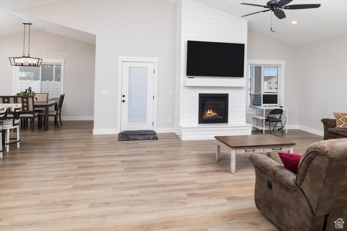 Living room with ceiling fan, a large fireplace, light wood-type flooring, and vaulted ceiling