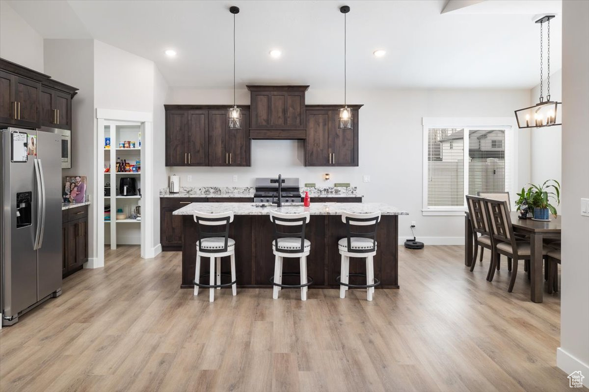 Kitchen with stainless steel appliances, dark brown cabinetry, a center island with sink, and hanging light fixtures