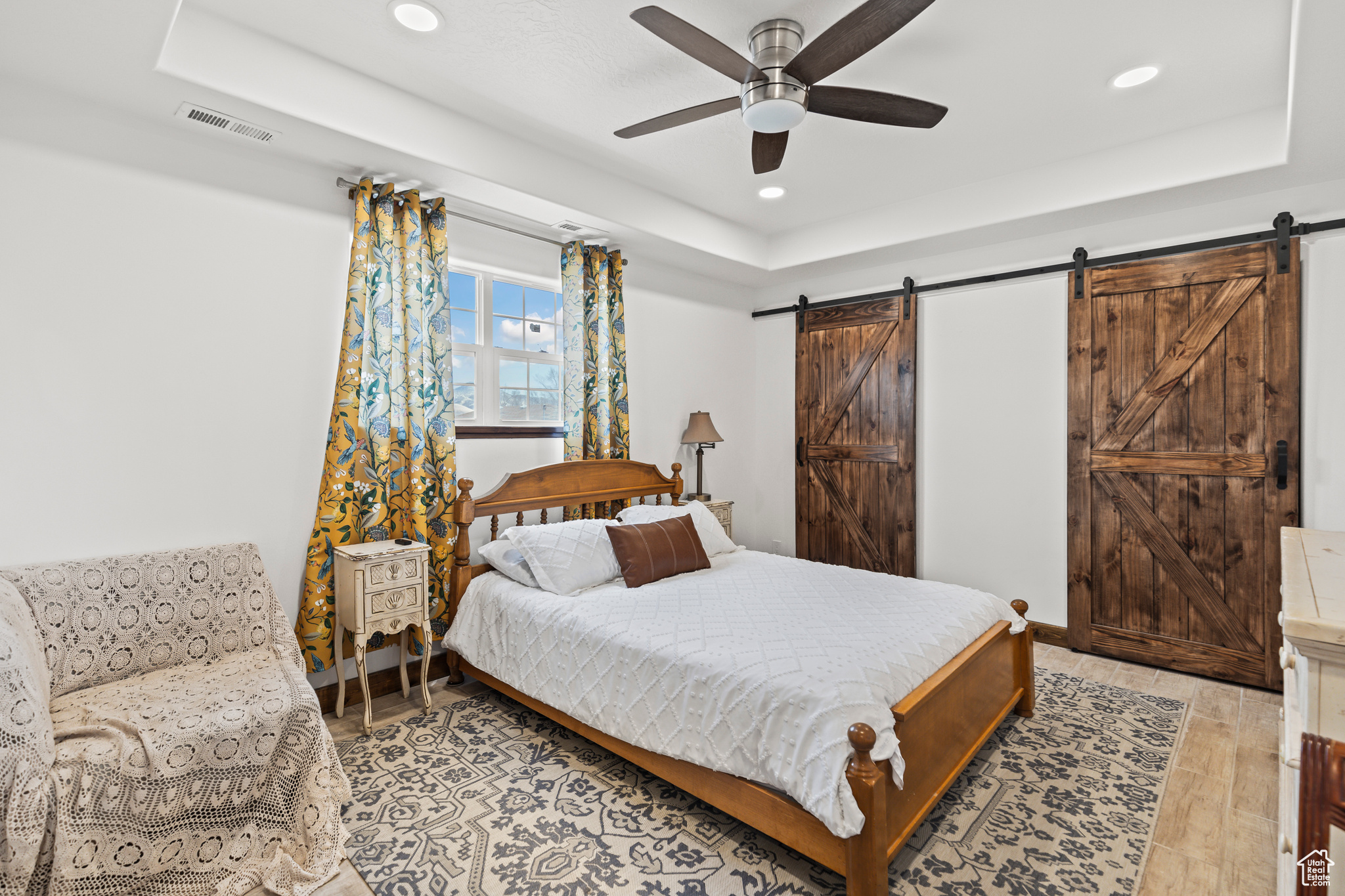 Bedroom featuring ceiling fan, a barn door, and a raised ceiling