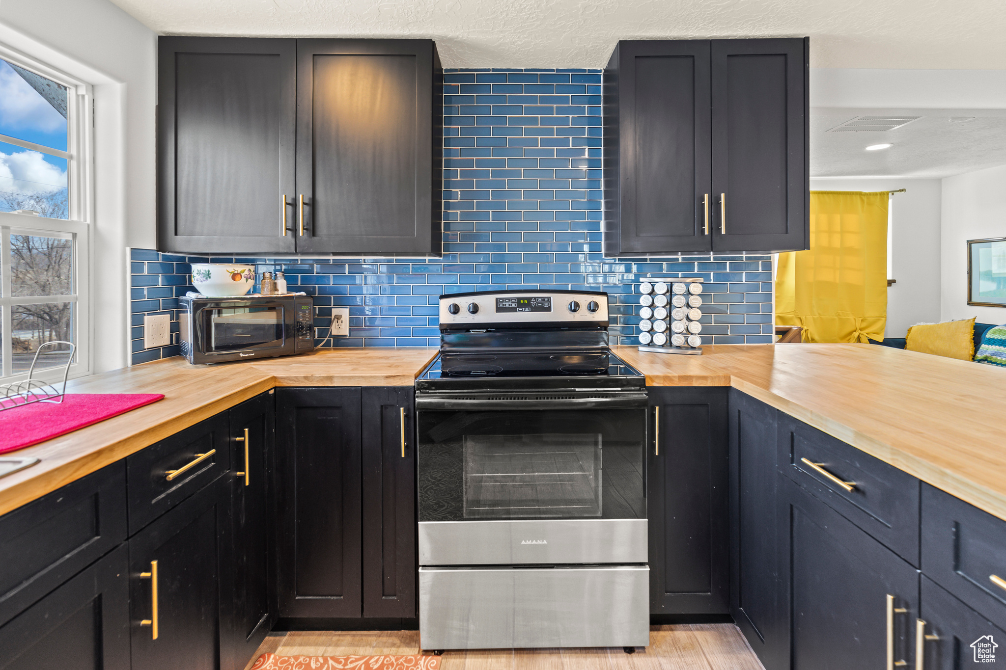 Kitchen with backsplash, butcher block counters, and stainless steel range with electric stovetop