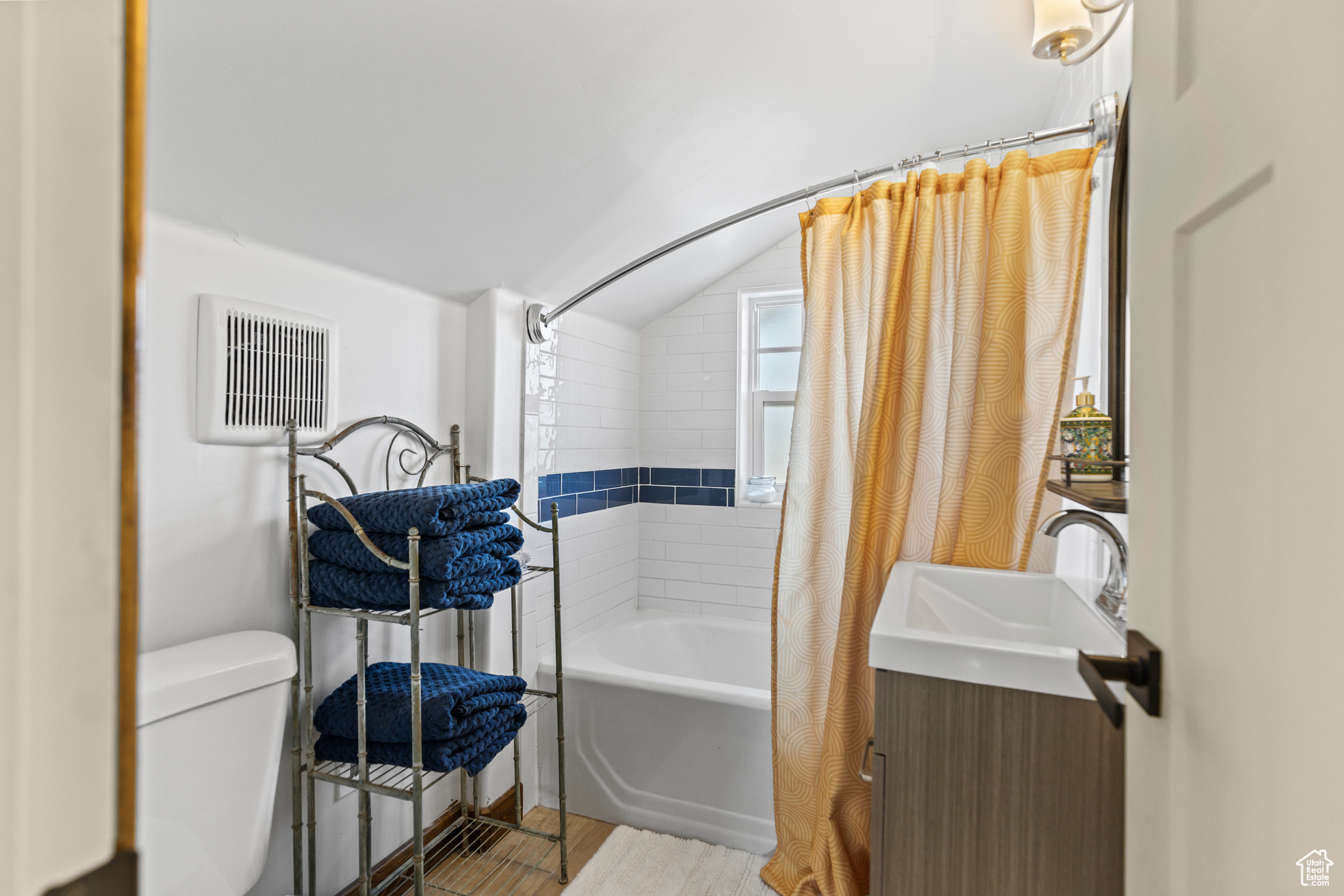 Full bathroom with lofted ceiling, vanity, toilet, and shower / bath combo with shower curtain